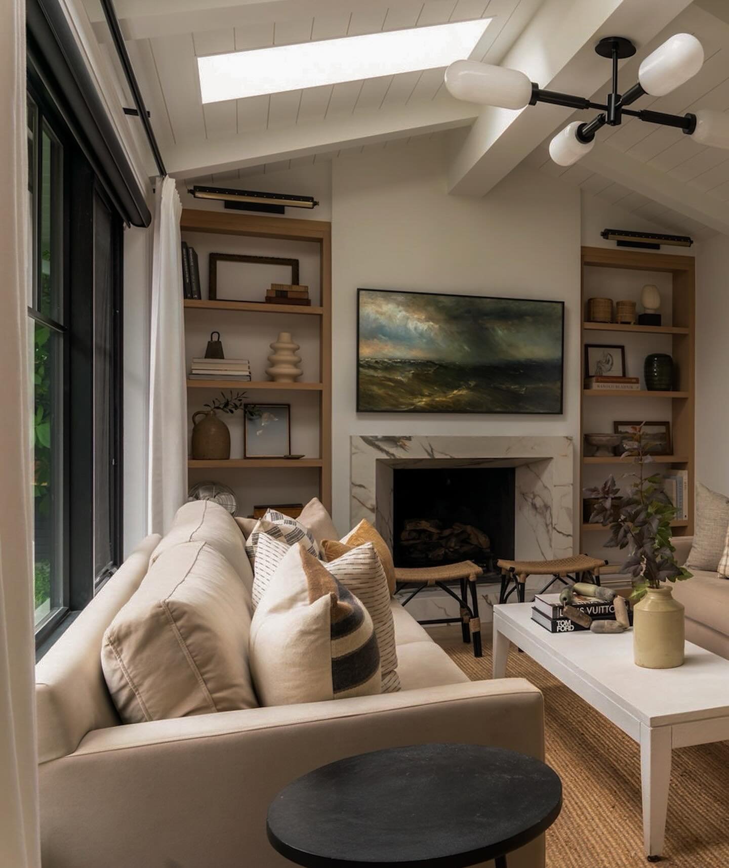 Tall wooden built-in shelves next to a marble fireplace with black picture lights