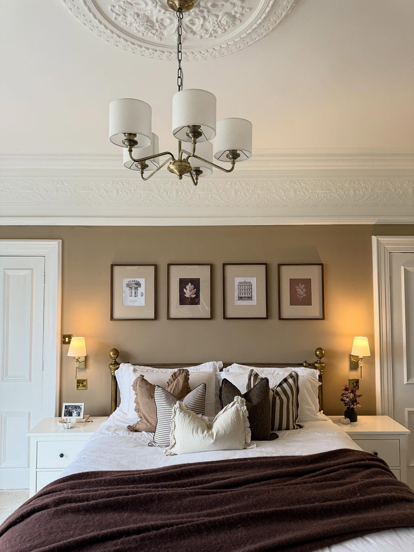 Bedroom featuring tan walls, intricate white ceiling molding, a brass bed frame, and a row of four framed prints