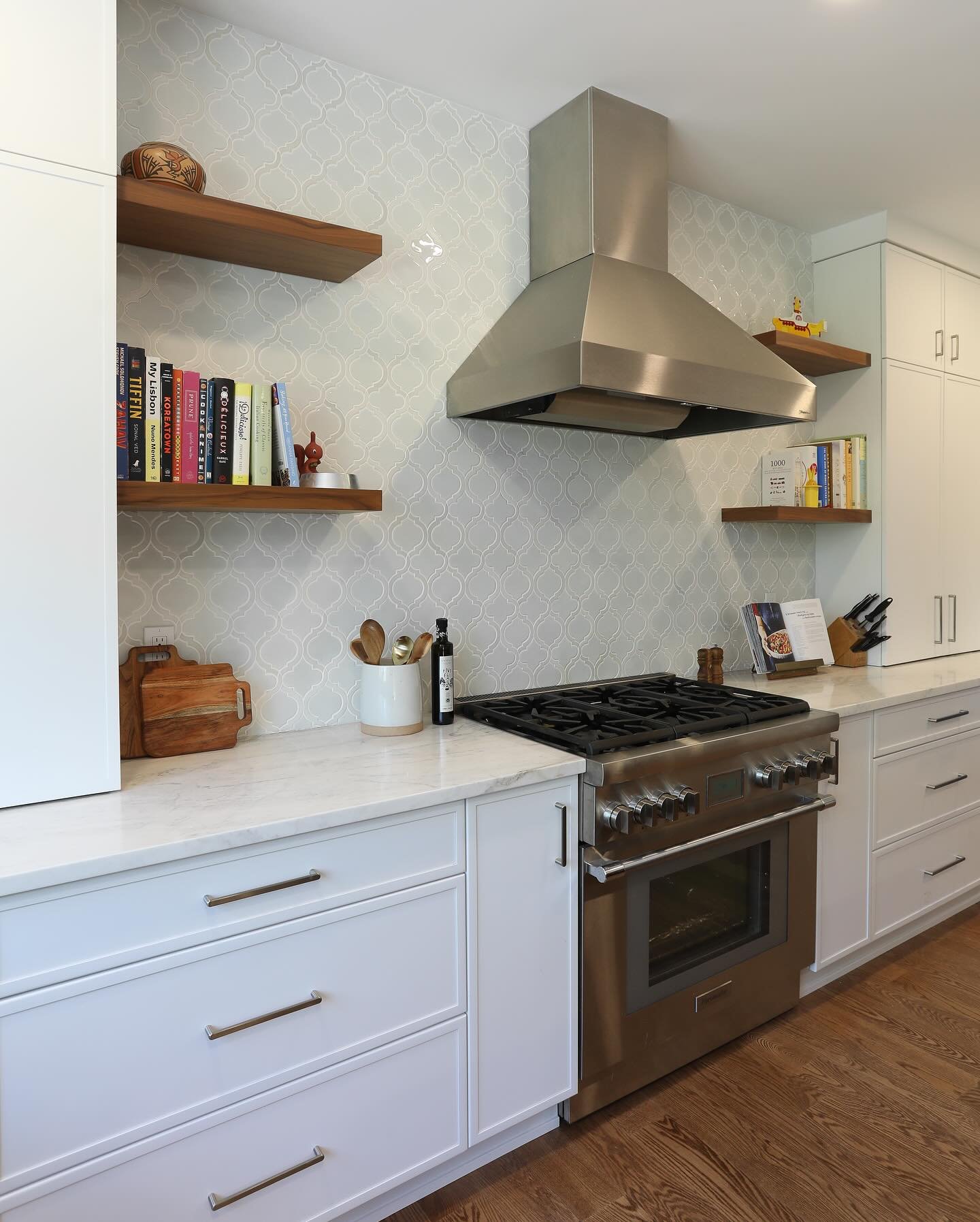 Wooden floating shelves placed symmetrically on either side of a stainless steel range hood in a modern kitchen.