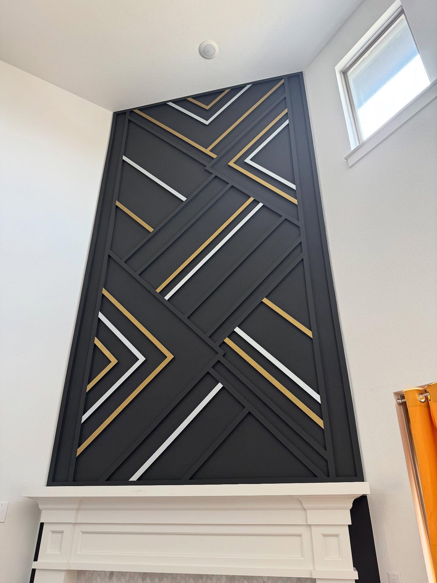 Tall fireplace accent wall featuring a complex, abstract geometric pattern painted matte black with metallic gold and white trim lines.