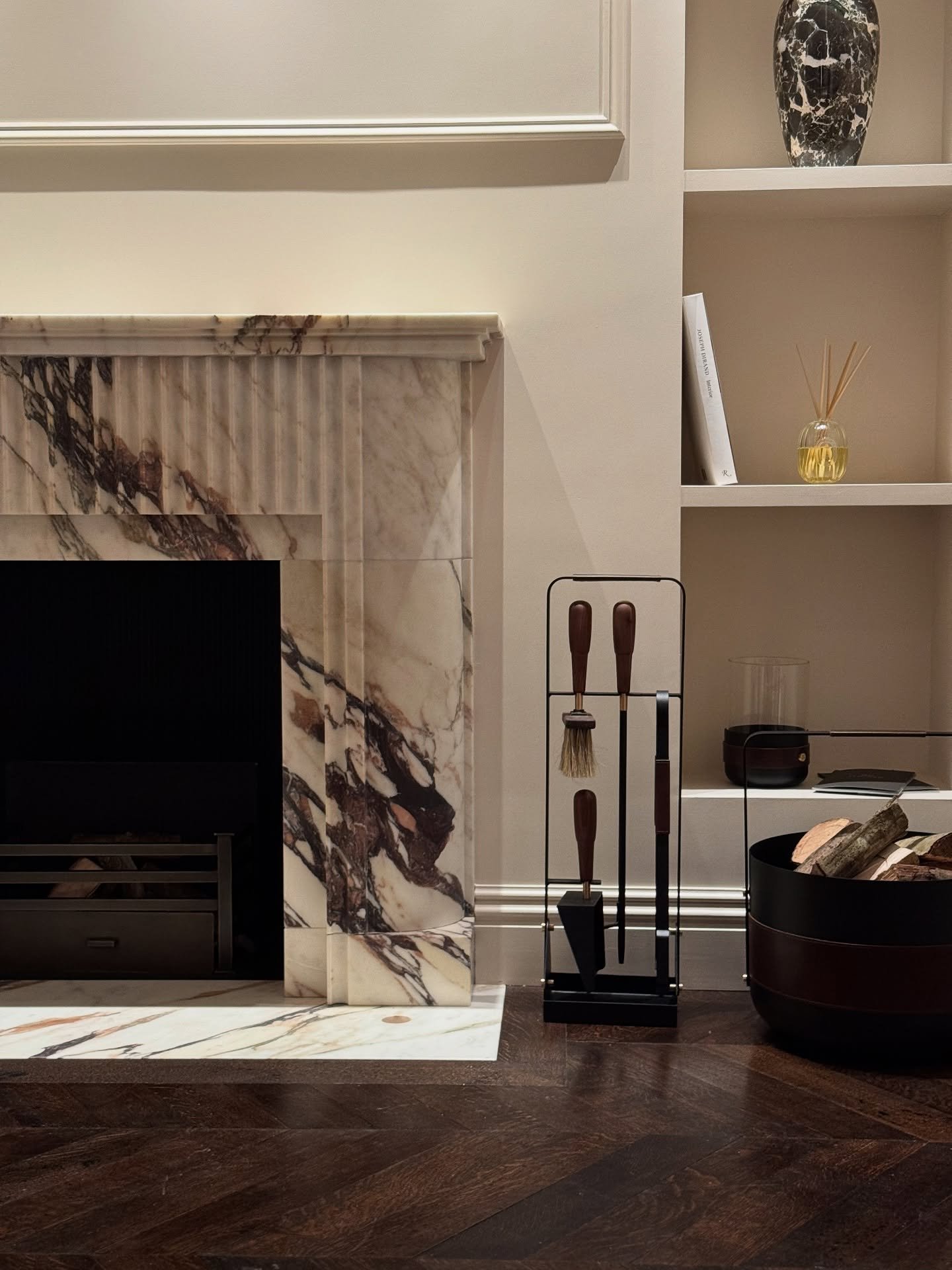 A traditional fireplace surround made of white marble with deep rust and brown veining, featuring a fluted vertical panel detail.