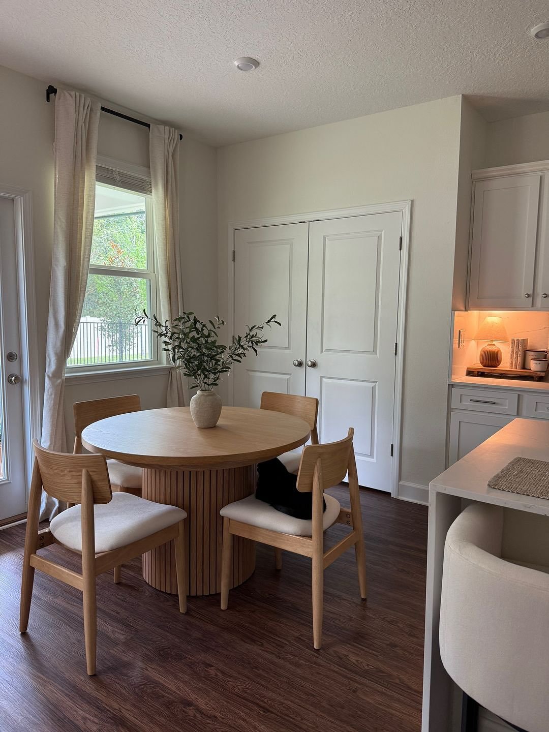 Round light wood dining table with ribbed cylinder base near window