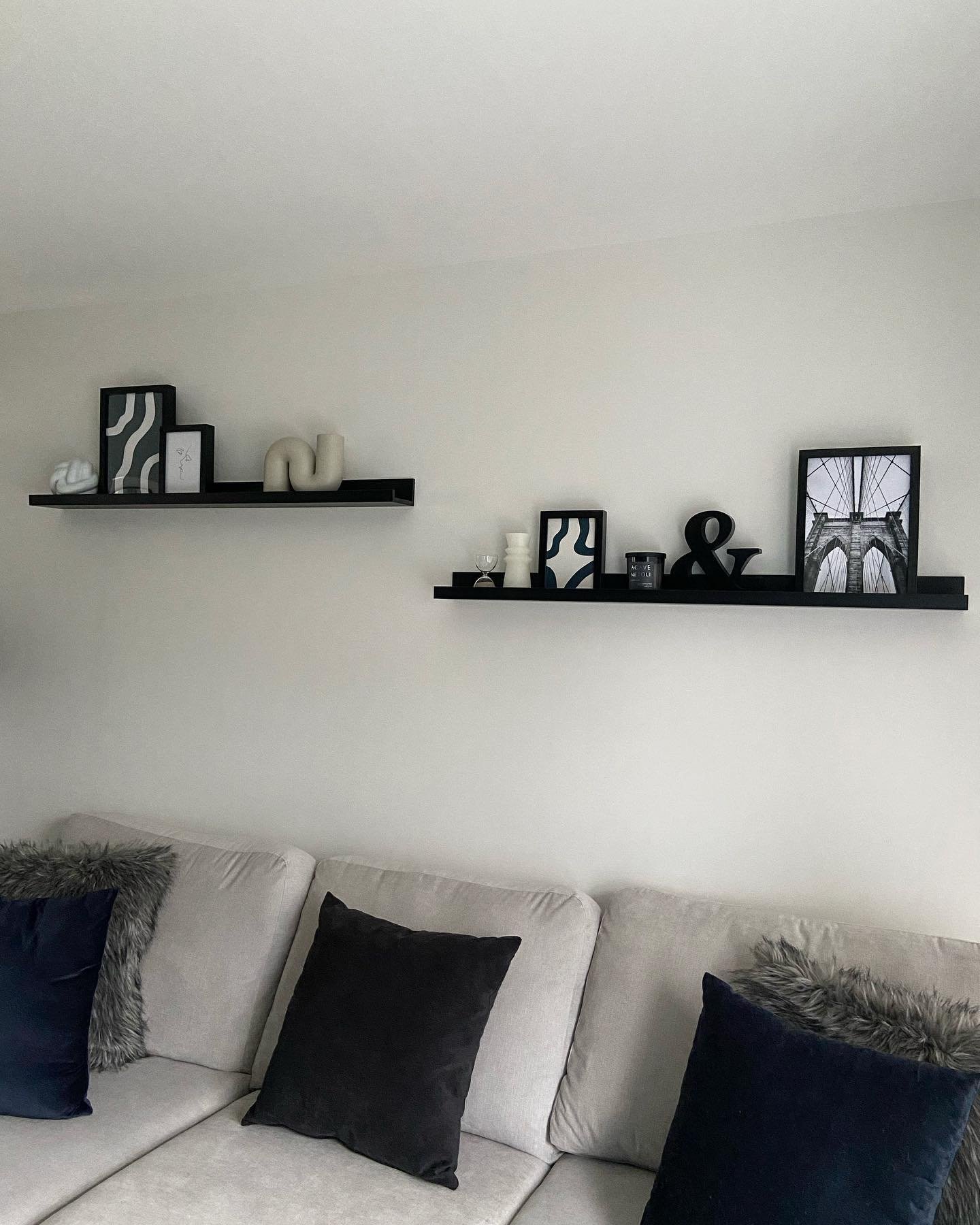 Staggered black picture ledges with monochrome decor above a grey couch