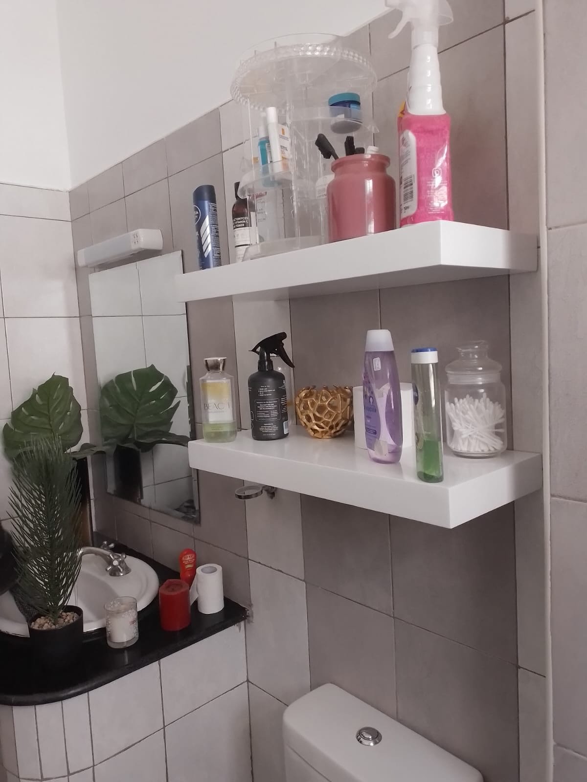 Two white glossy floating shelves mounted on grey bathroom tiles