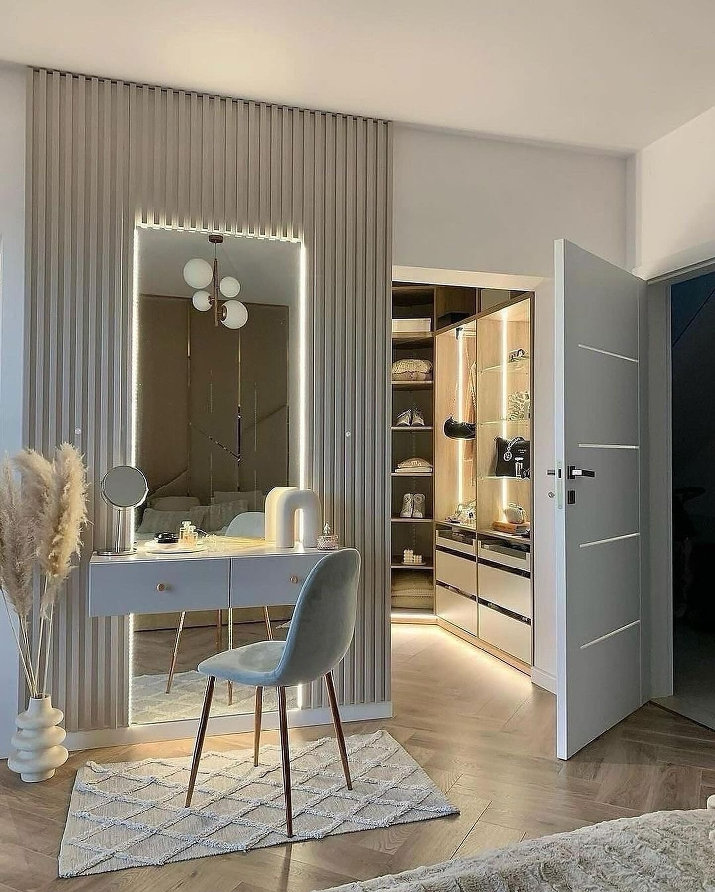 A bedroom corner featuring a modern vanity area with vertical slat wall paneling, a large backlit mirror, and a view into a small walk-in closet.