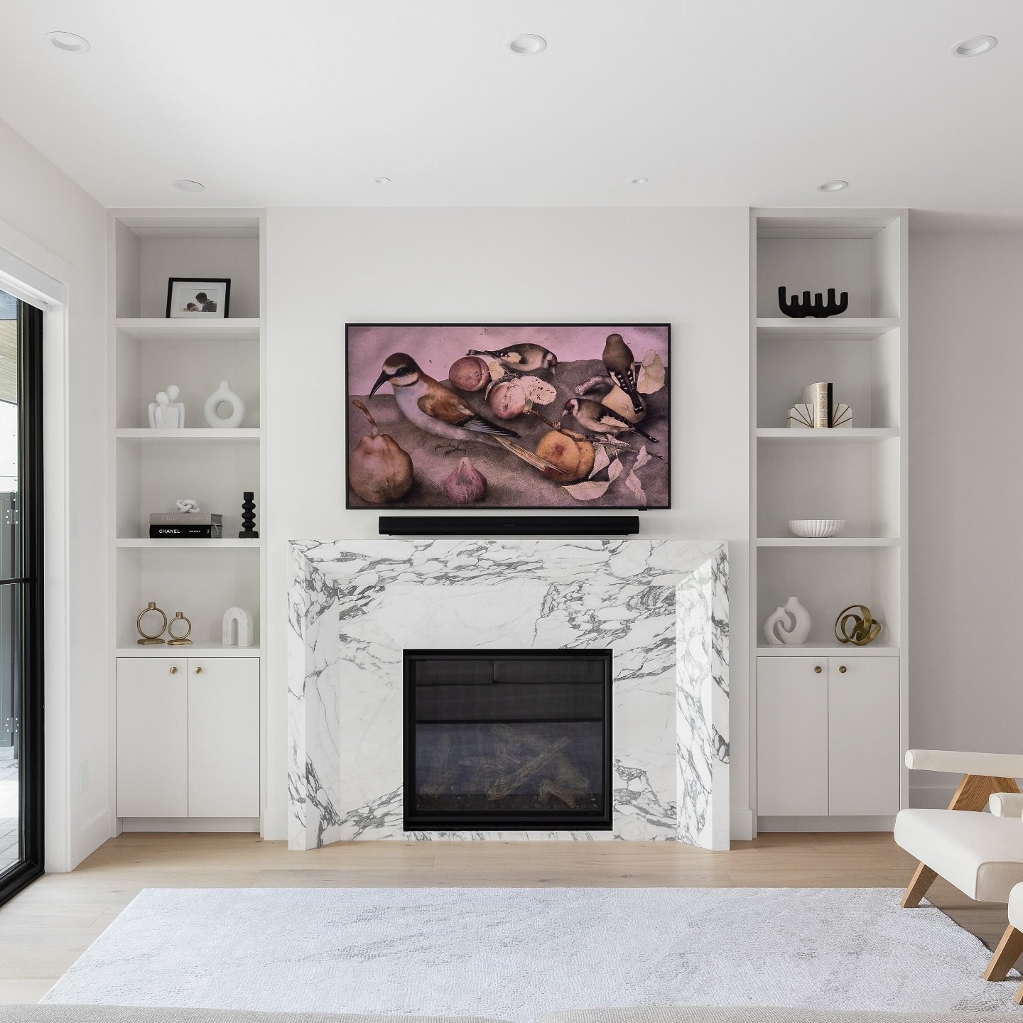 A modern, recessed fireplace with a thick, sharp white marble surround, integrated into a wall with symmetrical white built-in shelving.