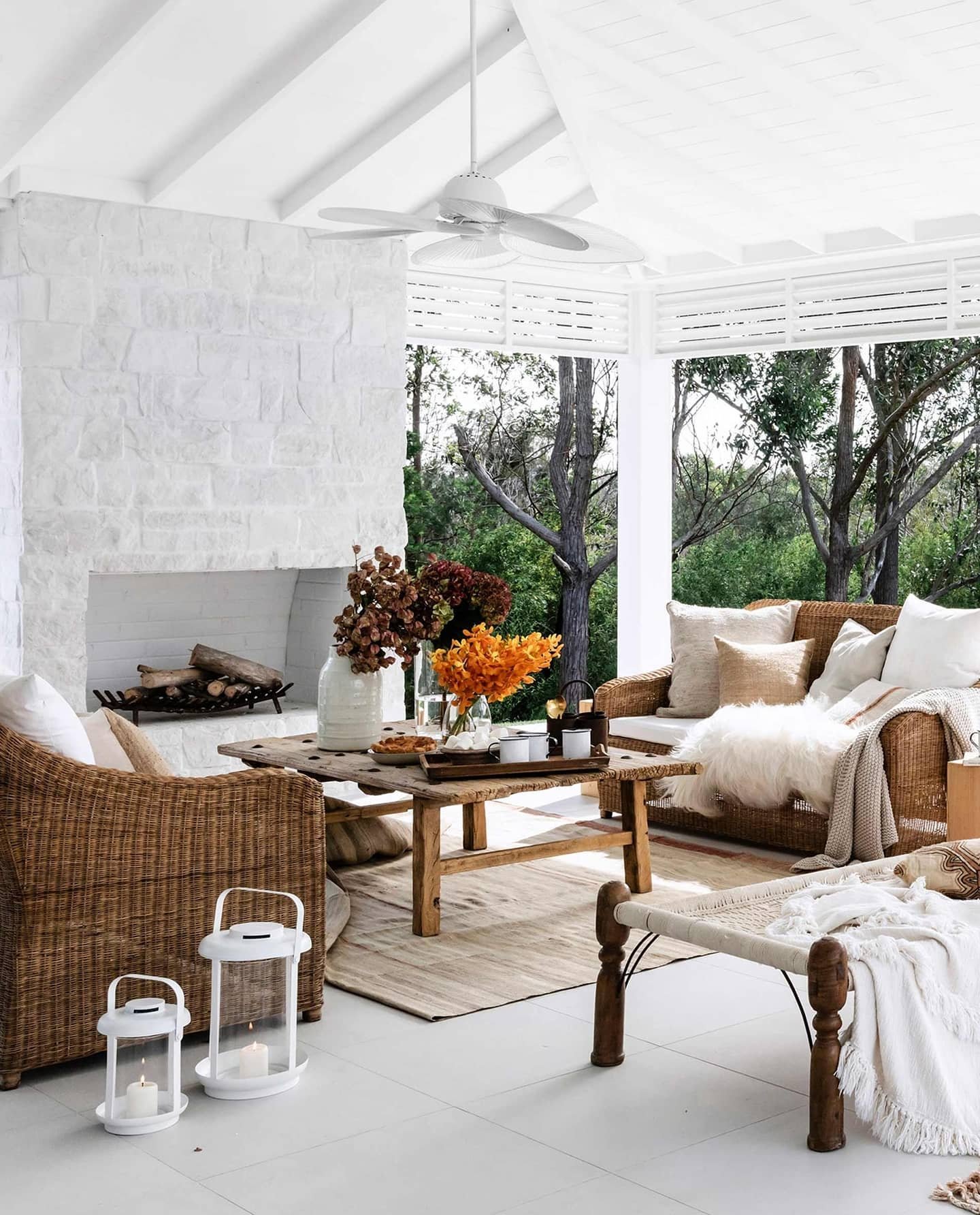 Rustic outdoor fireplace with a whitewashed stacked stone finish on a bright, all-white covered patio.