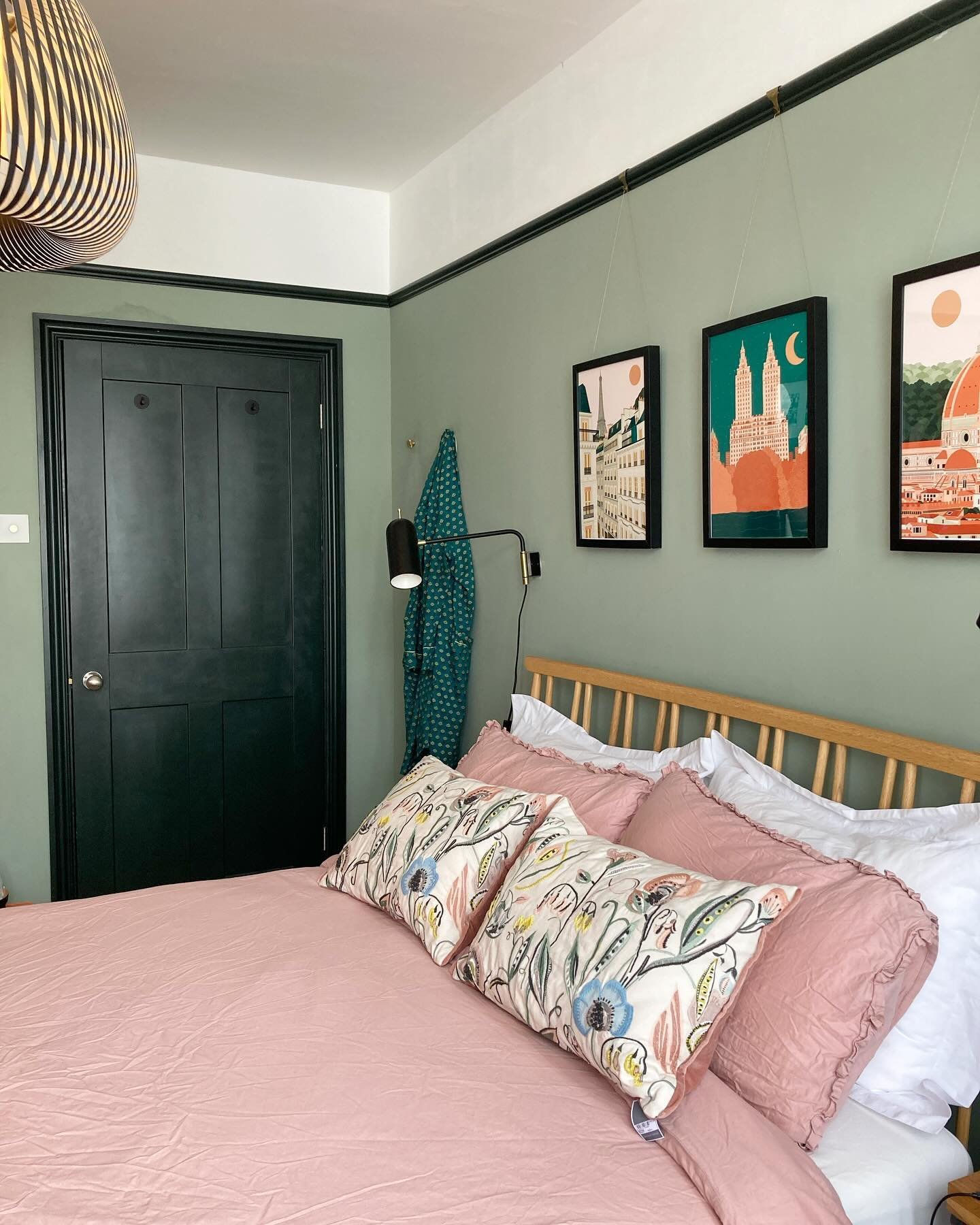 A bedroom featuring walls painted in a light sage green, a dark green door and picture rail trim, a natural wood headboard, and a large pink duvet.