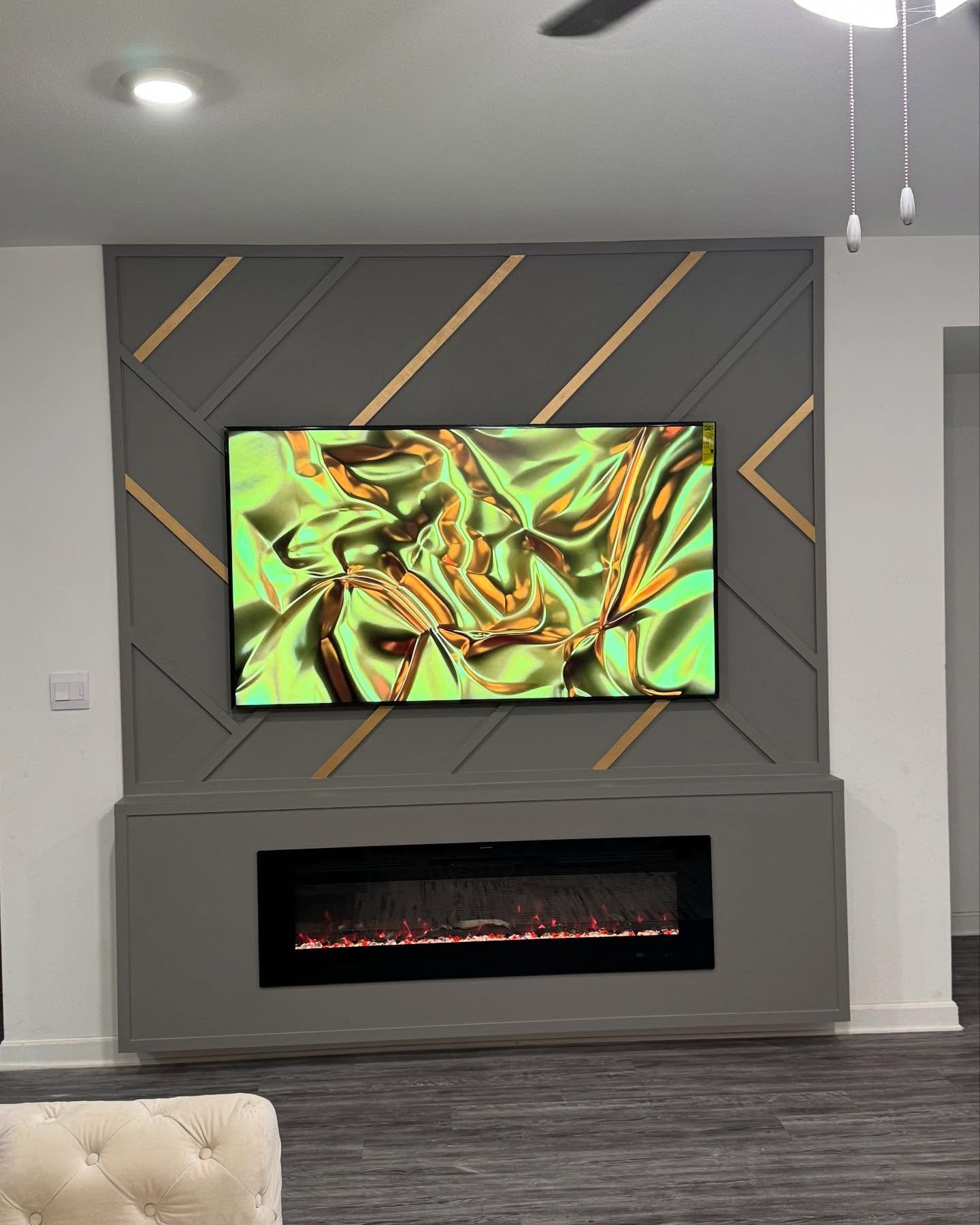 Modern living room featuring a linear electric fireplace and a charcoal gray accent wall with diagonal wood trim and thin gold strips.