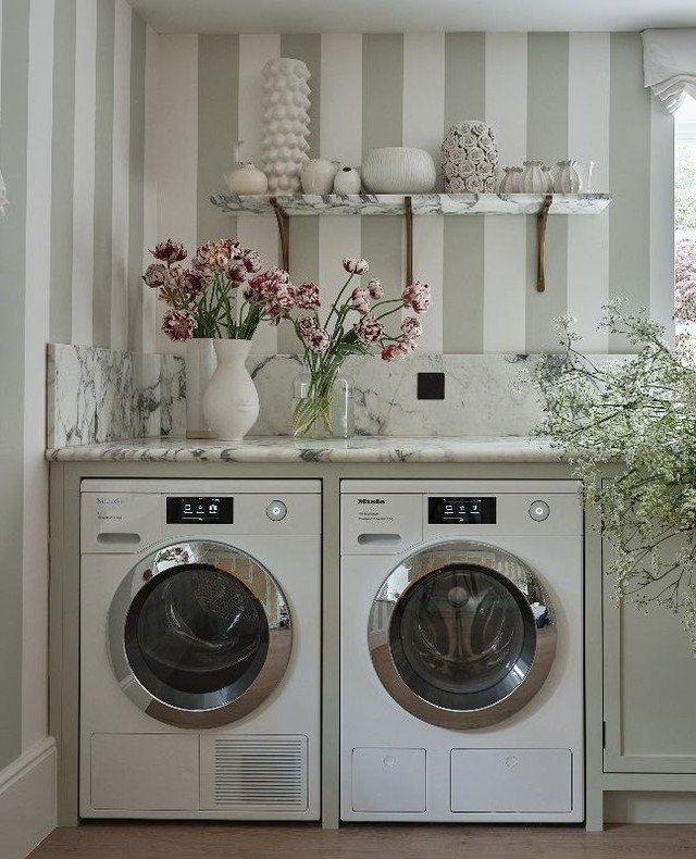 Single marble floating shelf with brass brackets holding vases above laundry machines