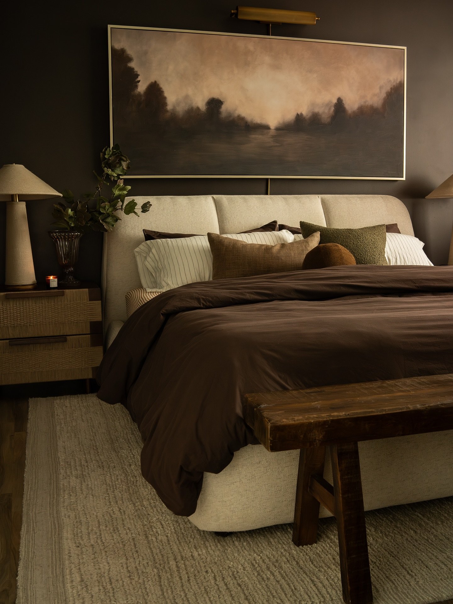 Brown bedroom featuring a rustic bench, dark bedding, and moody landscape wall art