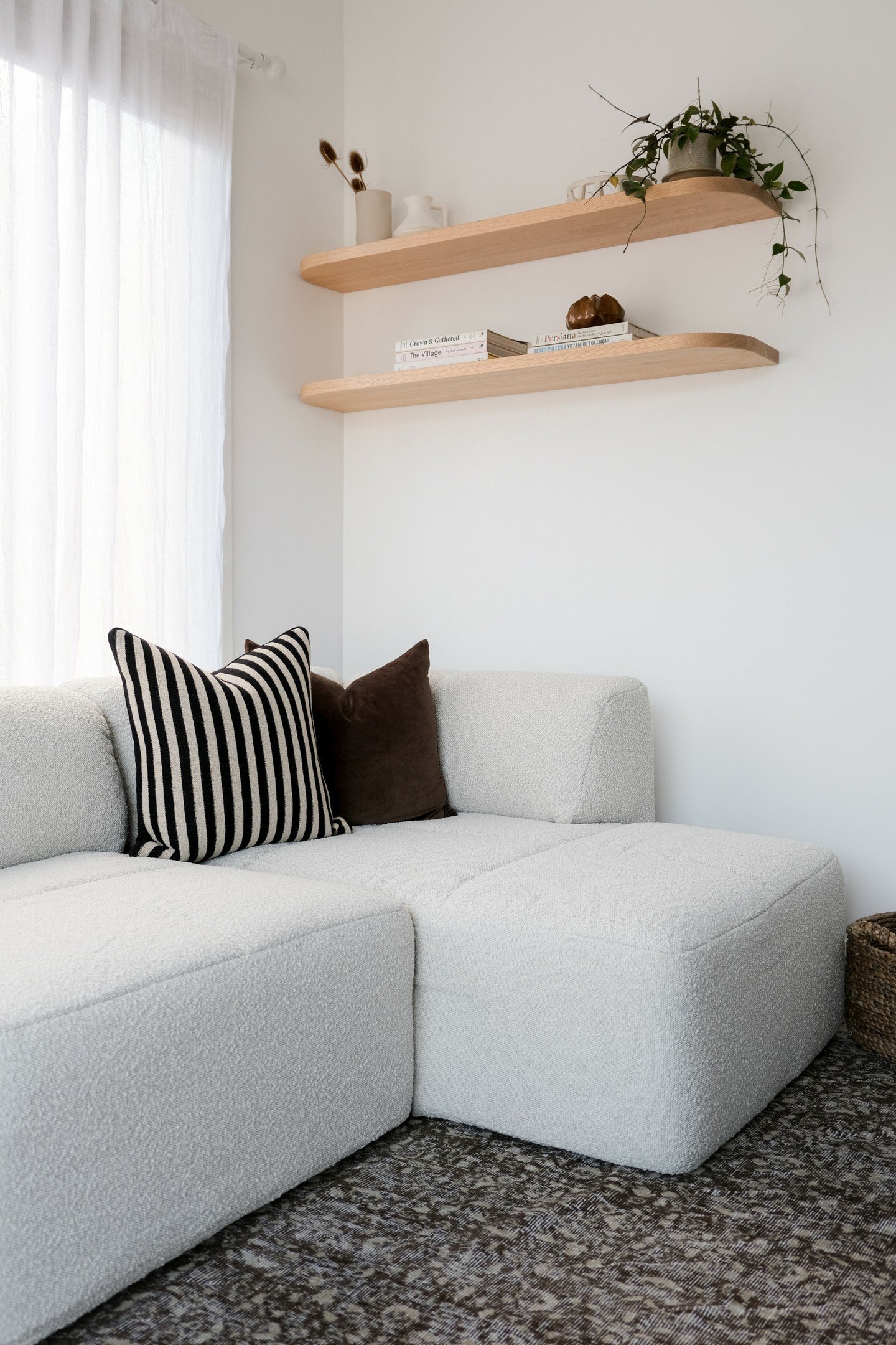 Two light wood floating shelves with rounded edges above a white sofa