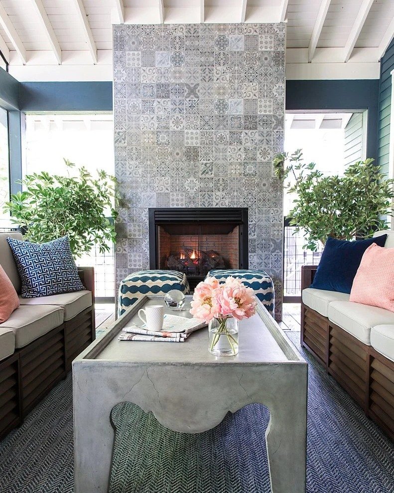 An outdoor covered porch with a fireplace that extends floor-to-ceiling, covered in a mix of gray and white patterned patchwork cement tiles.