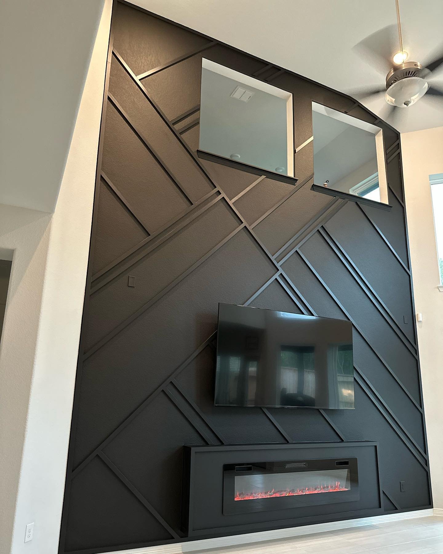 Floor-to-ceiling matte black accent wall with a complex intersecting geometric trim pattern, featuring a modern linear fireplace.
