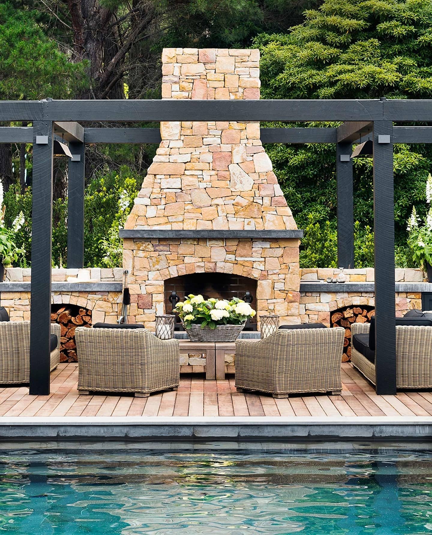 Tall, rustic outdoor fireplace made of large, irregularly shaped, multi-colored fieldstones set between black pergola posts.