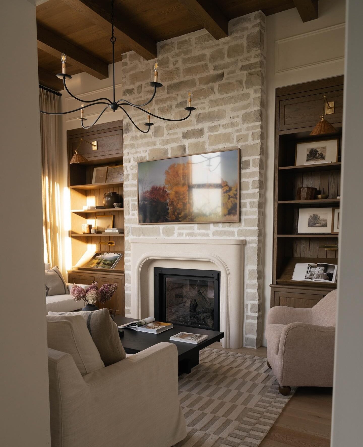 A tall, floor-to-ceiling fireplace made of light-colored, roughly cut stone, featuring a smooth, pale stone firebox surround, flanked by built-in dark wood bookshelves, and with a television mounted above the mantel