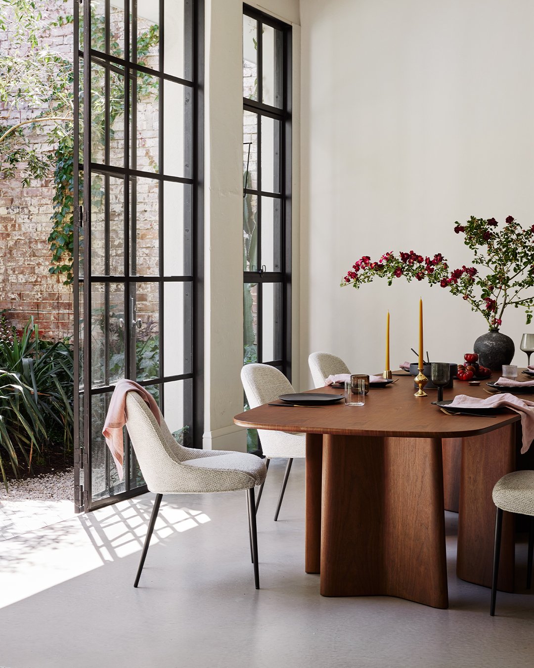 Walnut dining table with curved panel legs next to open garden doors