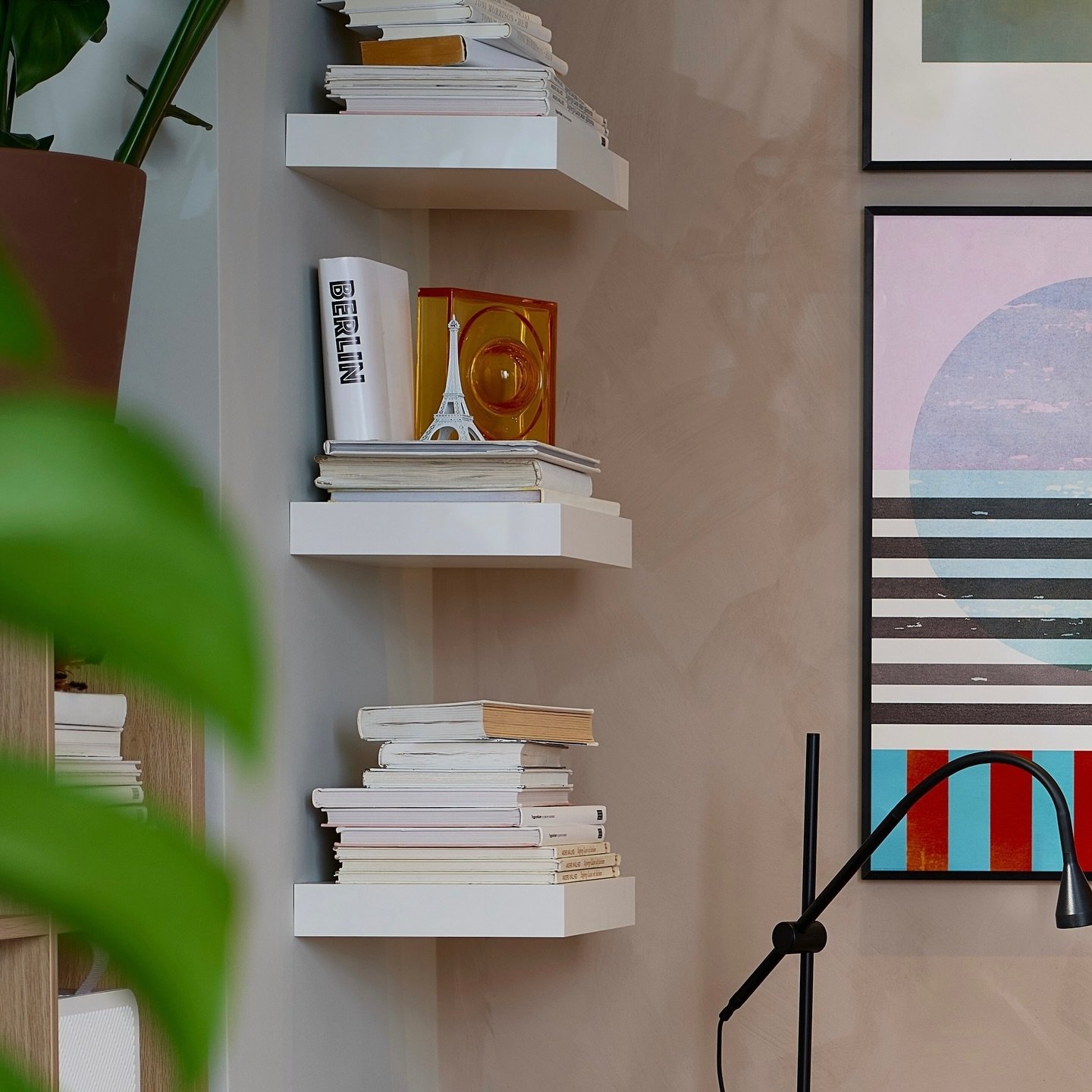 Three thick white square floating shelves mounted vertically on a grey painted wall corner holding books.