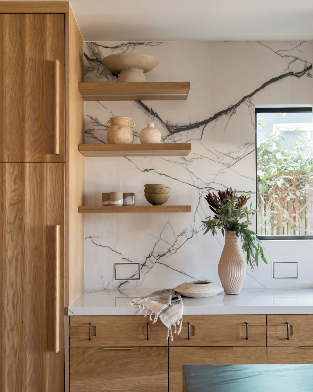 Sleek wood floating shelves mounted on a striking black and white marble slab backsplash.