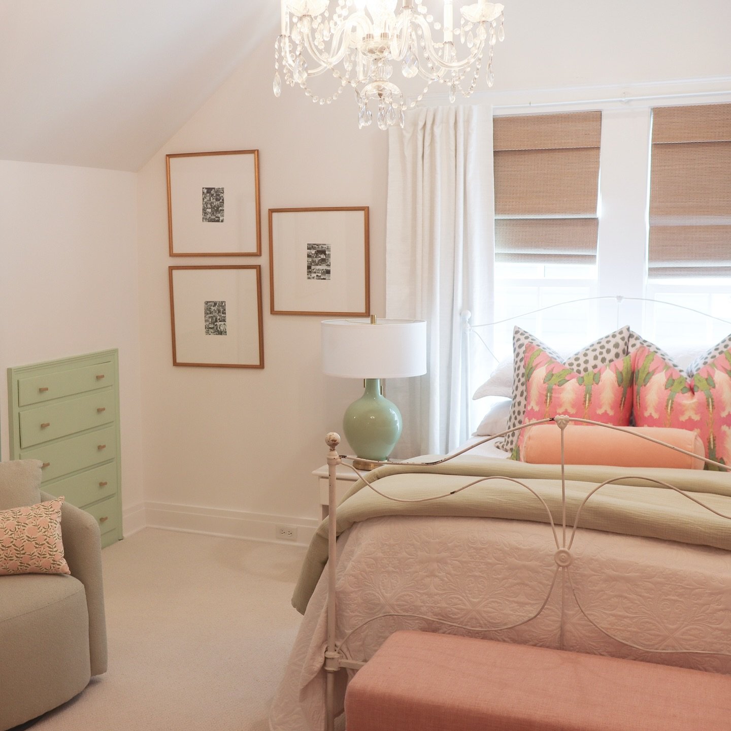 A bright bedroom with a sloped ceiling, featuring a mint green dresser, a white metal bed, and decorative pillows in coral, pink, and green prints.