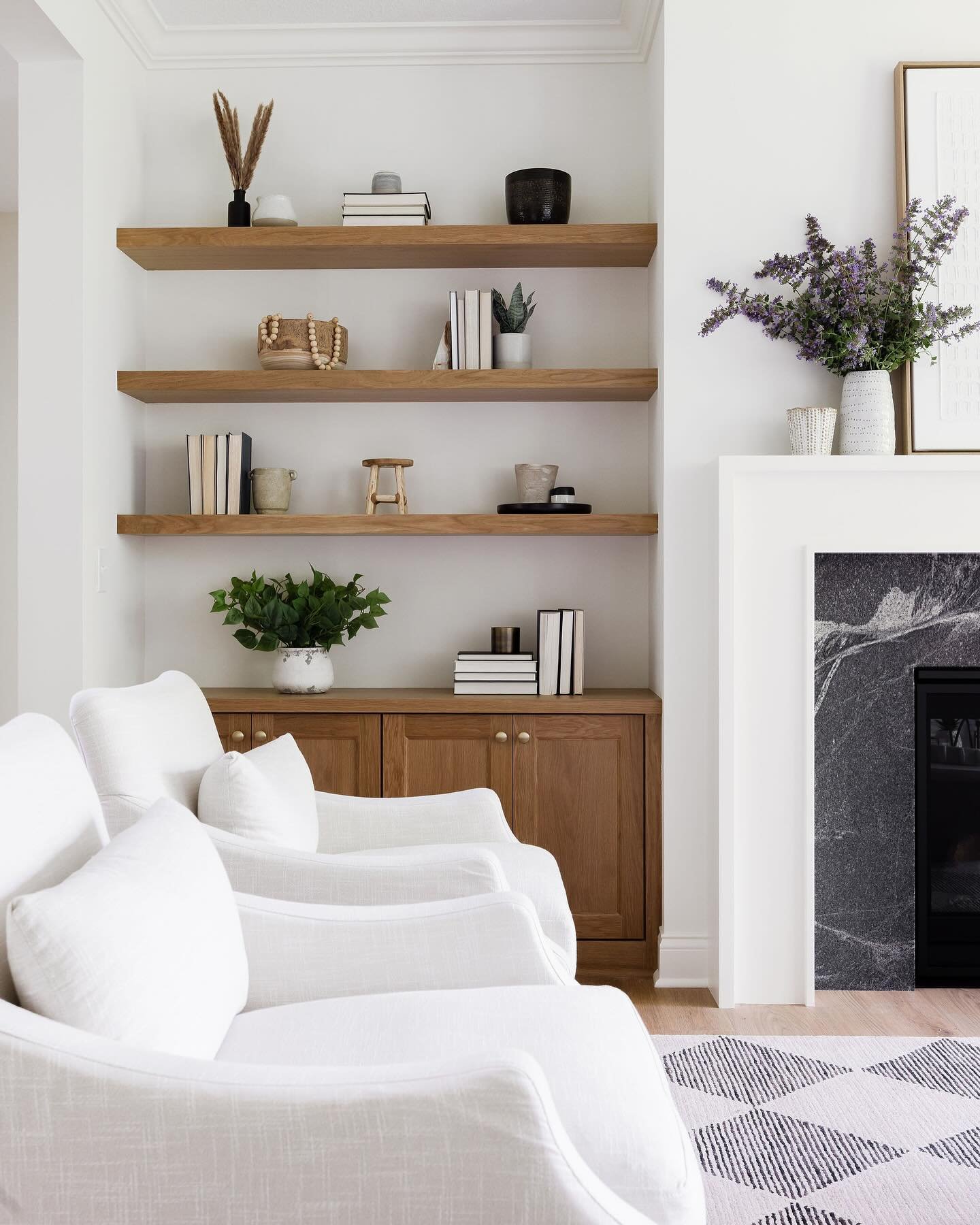 Light oak floating shelves and cabinets built into a white living room niche