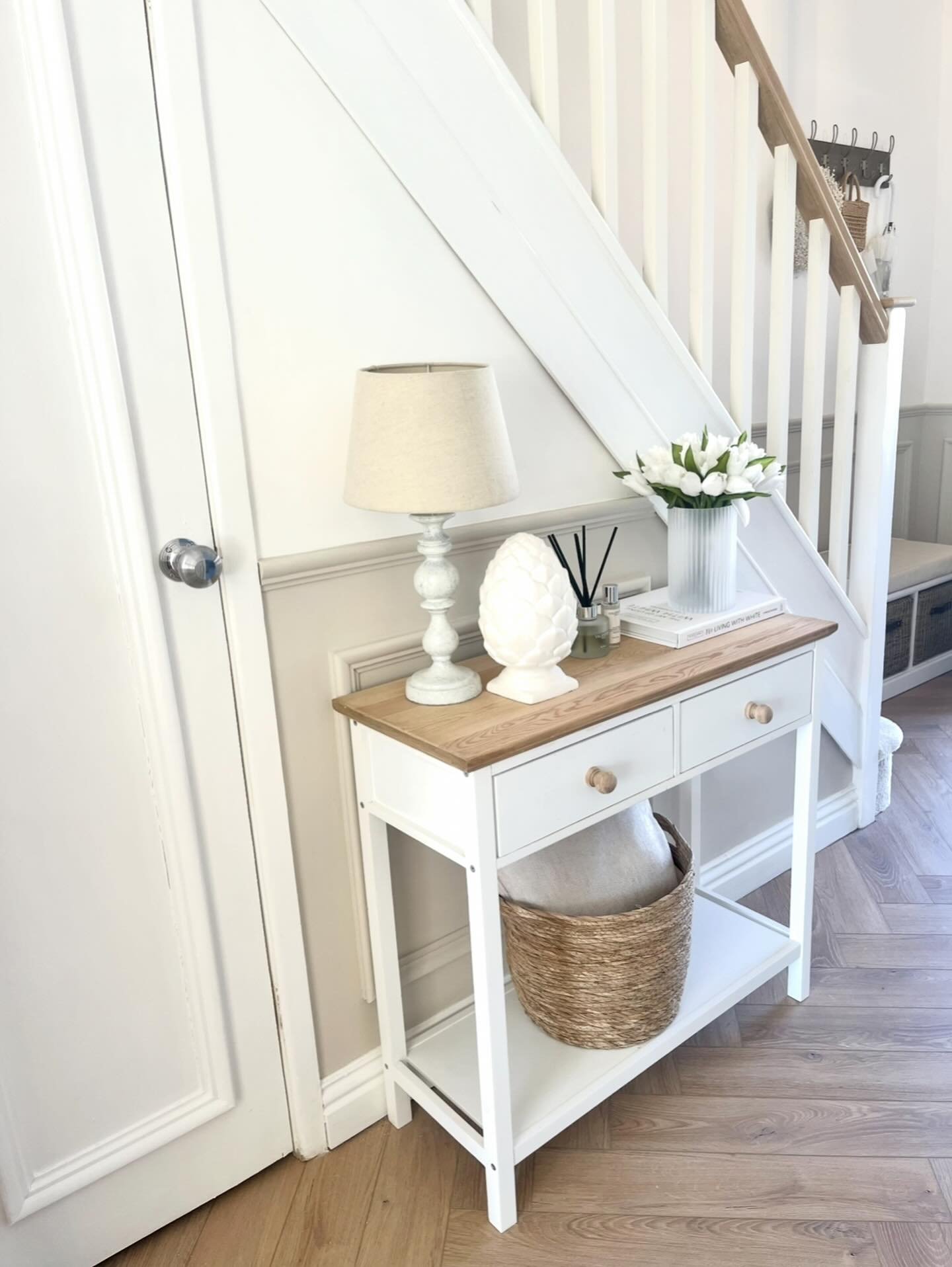 Small white hallway table under stairs with wicker basket