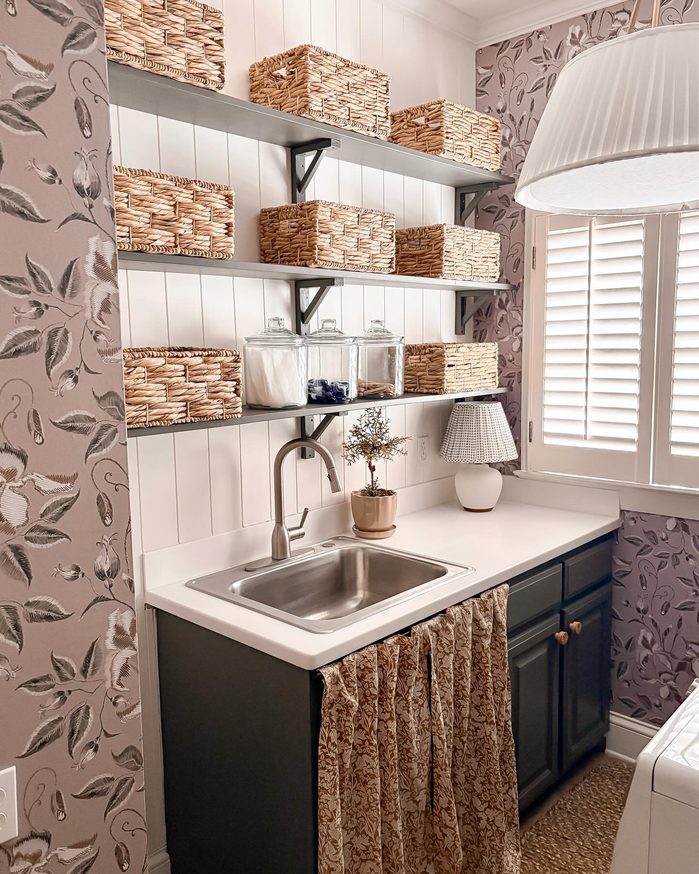 Dark grey shelves on white beadboard wall holding woven baskets and glass jars above a sink