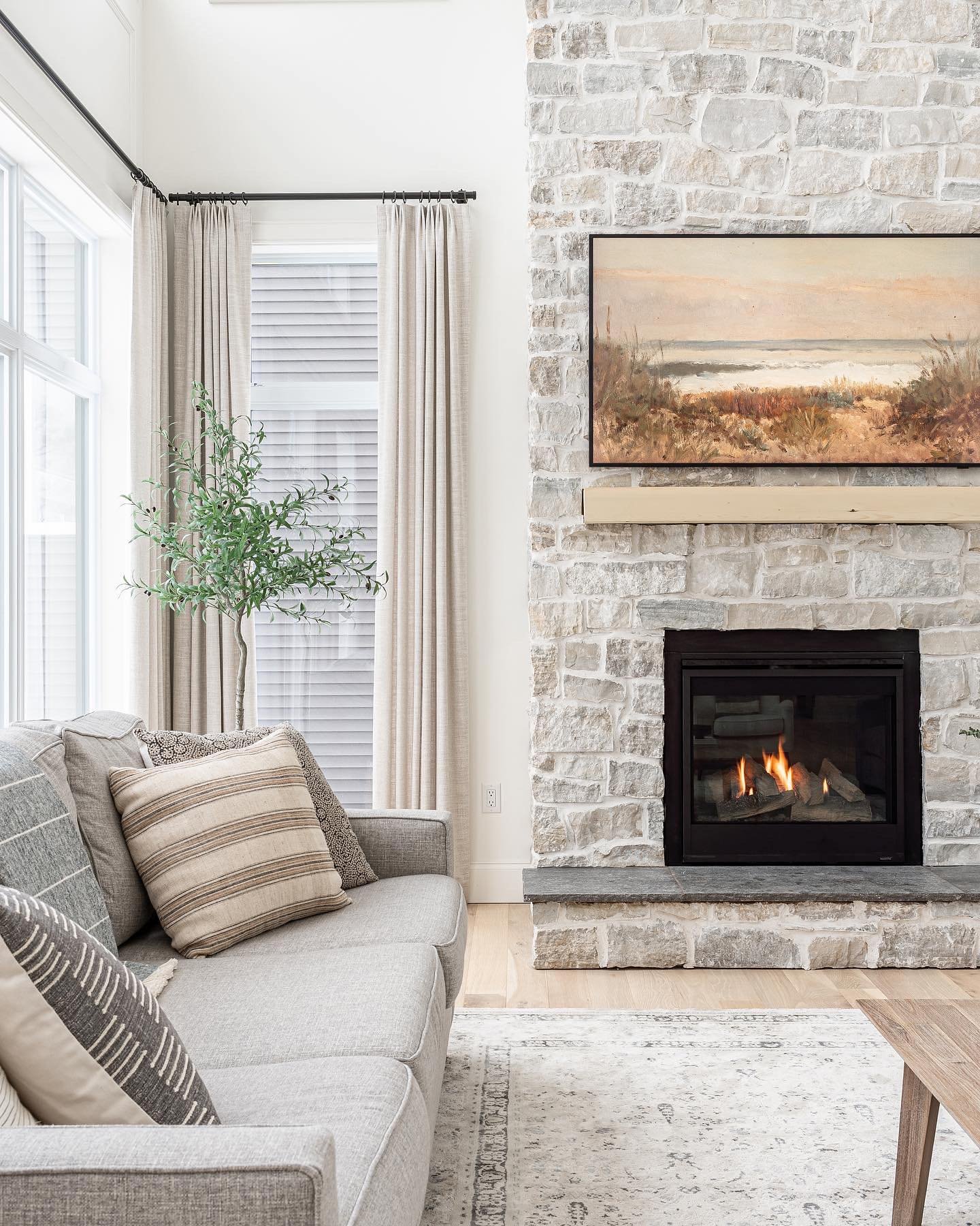 A tall, floor-to-ceiling fireplace made of light grey and white rectangular-cut stone, featuring a simple wood mantel, a black firebox insert, and an abstract landscape painting mounted above.