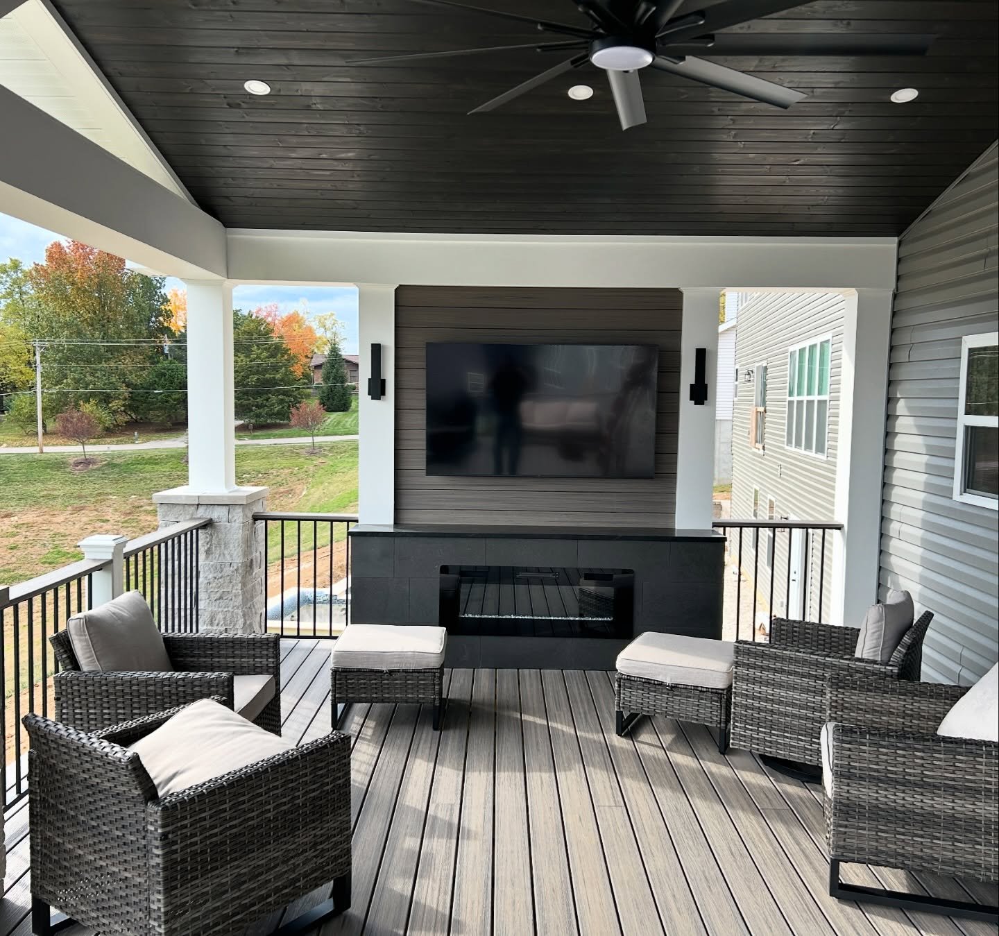 Horizontal, modern linear gas fireplace framed by black slate against a dark wood accent wall on a covered porch.