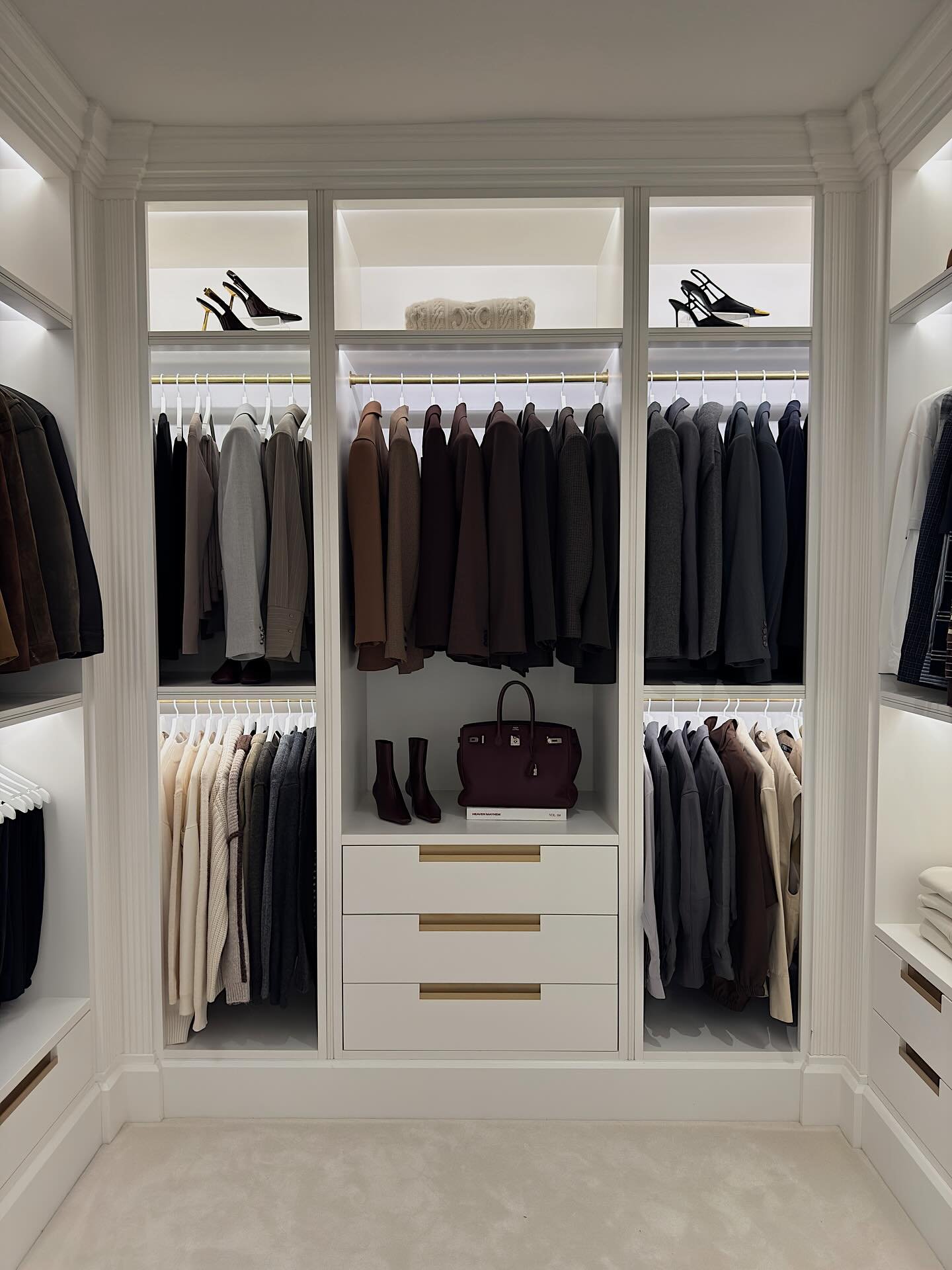 A symmetrical walk-in closet featuring white cabinetry, multiple hanging sections for organized clothing, and minimalist gold handles on drawers.