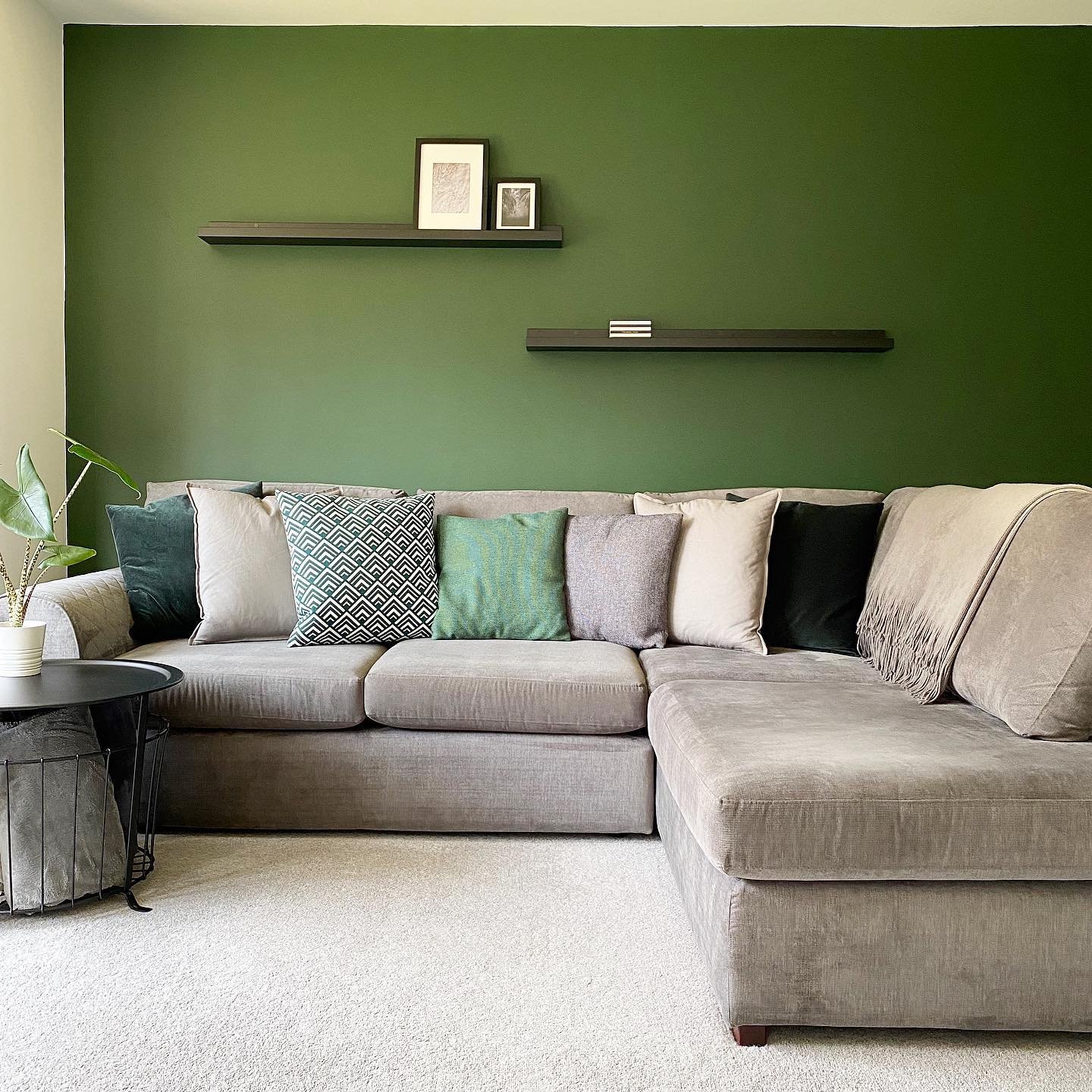 Two slim black floating shelves on a dark green wall above a grey sectional