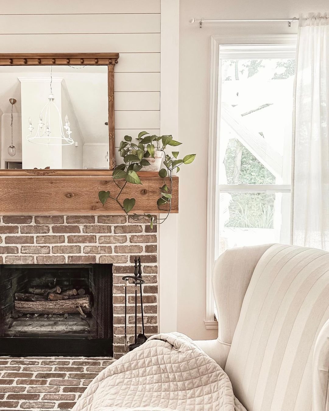 This fireplace features natural red brick with a very light, subtle whitewash application.The brickwork has a charming, weathered patina that suggests age and character.It includes a full brick hearth that extends outward, providing practical, rustic seating space.The masonry stops neatly at the mantel line, letting the chunky wood beam stand out.This simple, exposed brick adds timeless, cozy texture to the bright, shiplap-paneled wall.