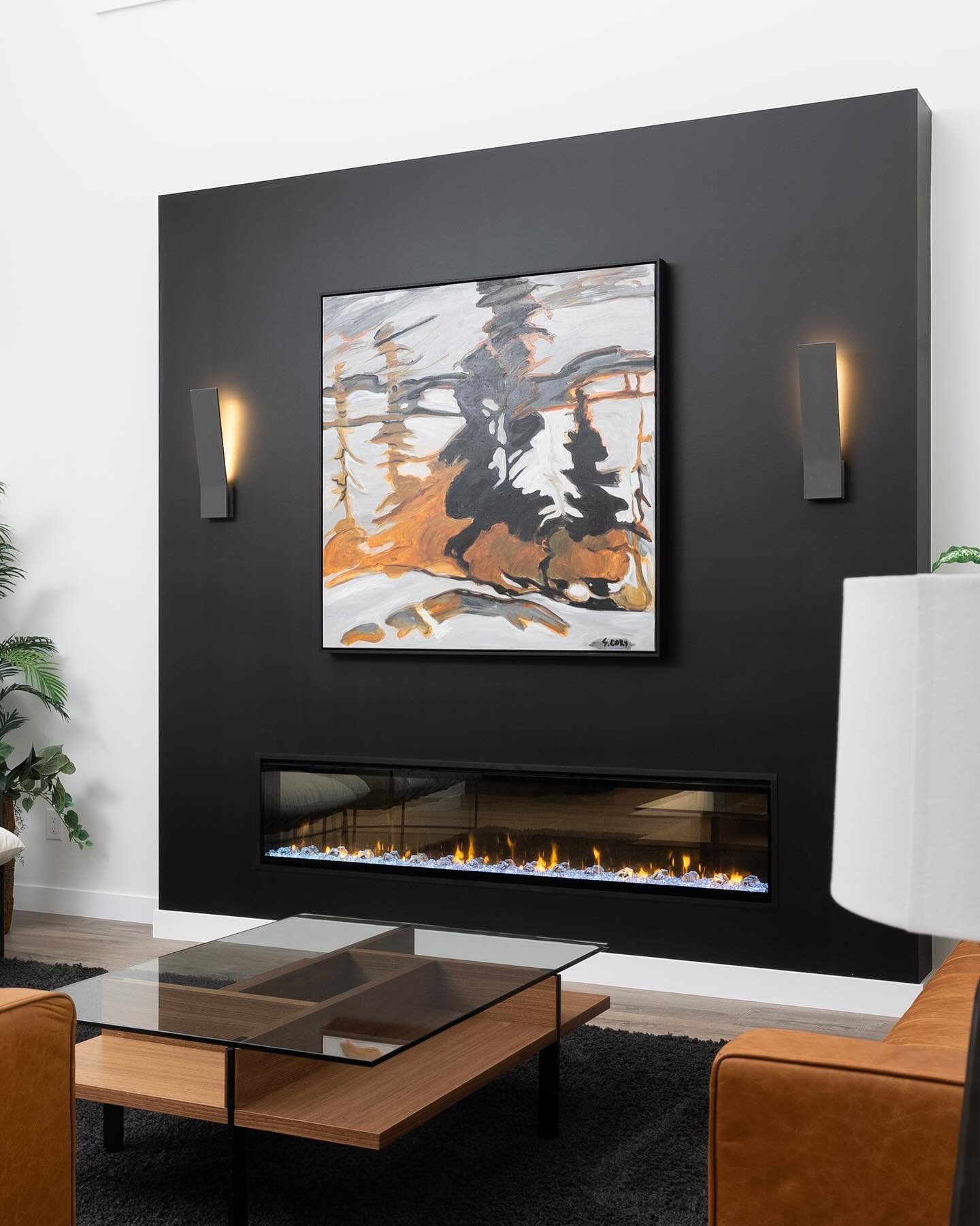 Minimalist living room with a linear electric fireplace and a large, floating black accent box wall centered with abstract artwork and sconces.