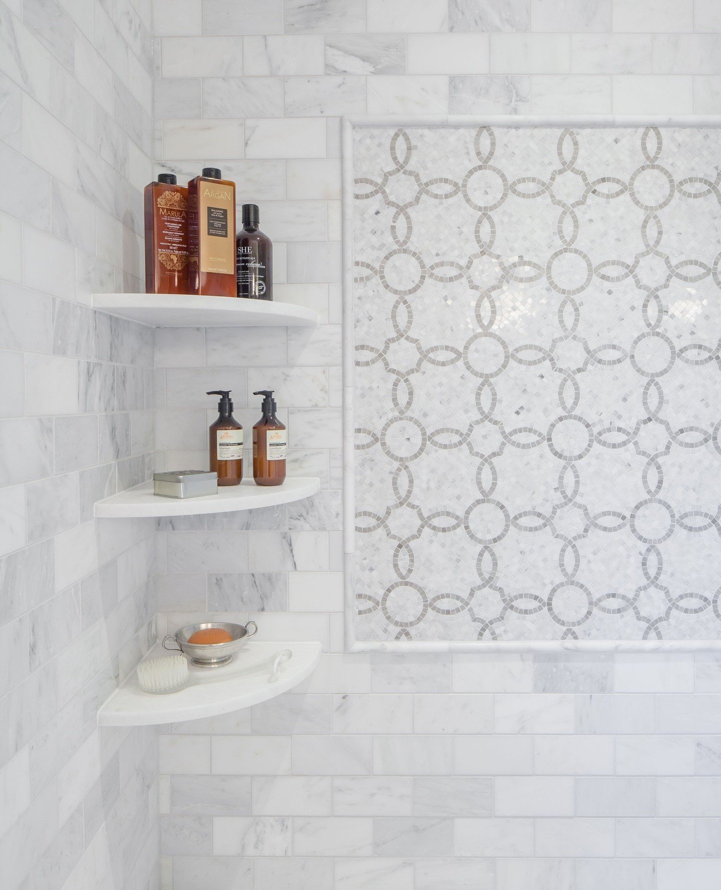 Three white curved-front corner shelves installed inside a marble-tiled shower stall.