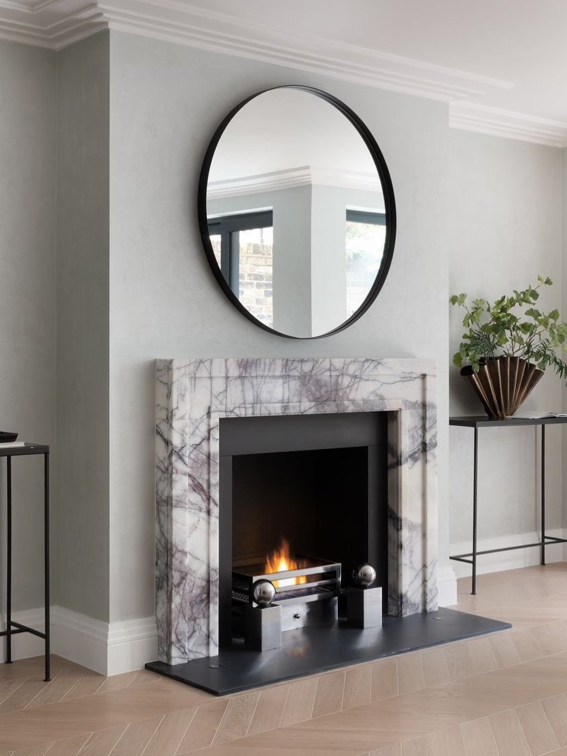 A traditional-style fireplace surround crafted from white marble with prominent purple and grey veining, contrasting with a round black mirror and dark hearth.