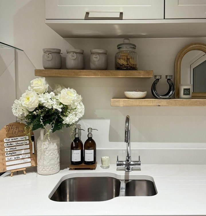 Two light wood floating shelves staggered above a kitchen sink, holding canisters and decor.