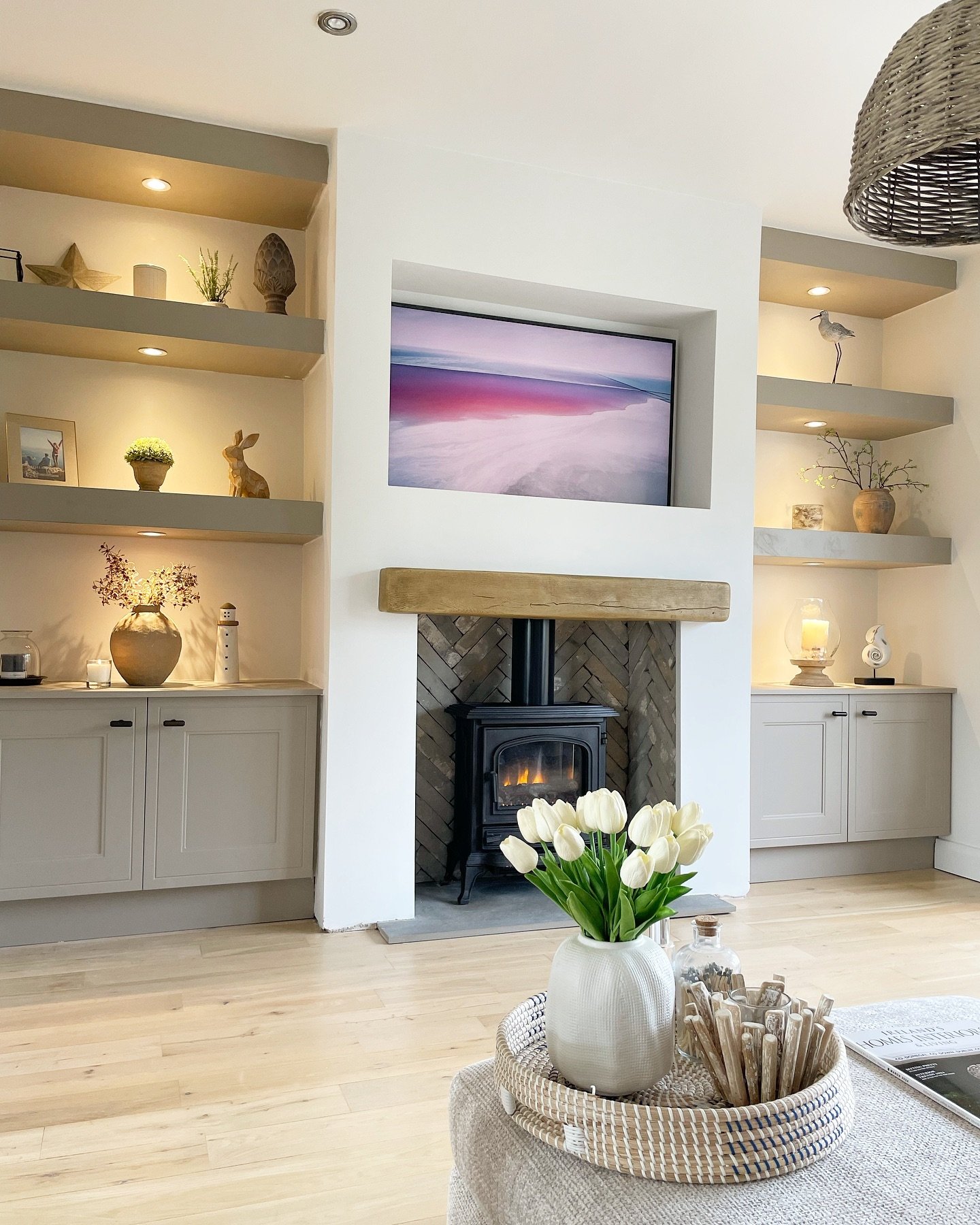 Grey built-in shelves with downlights flanking a white fireplace with a recessed TV.
