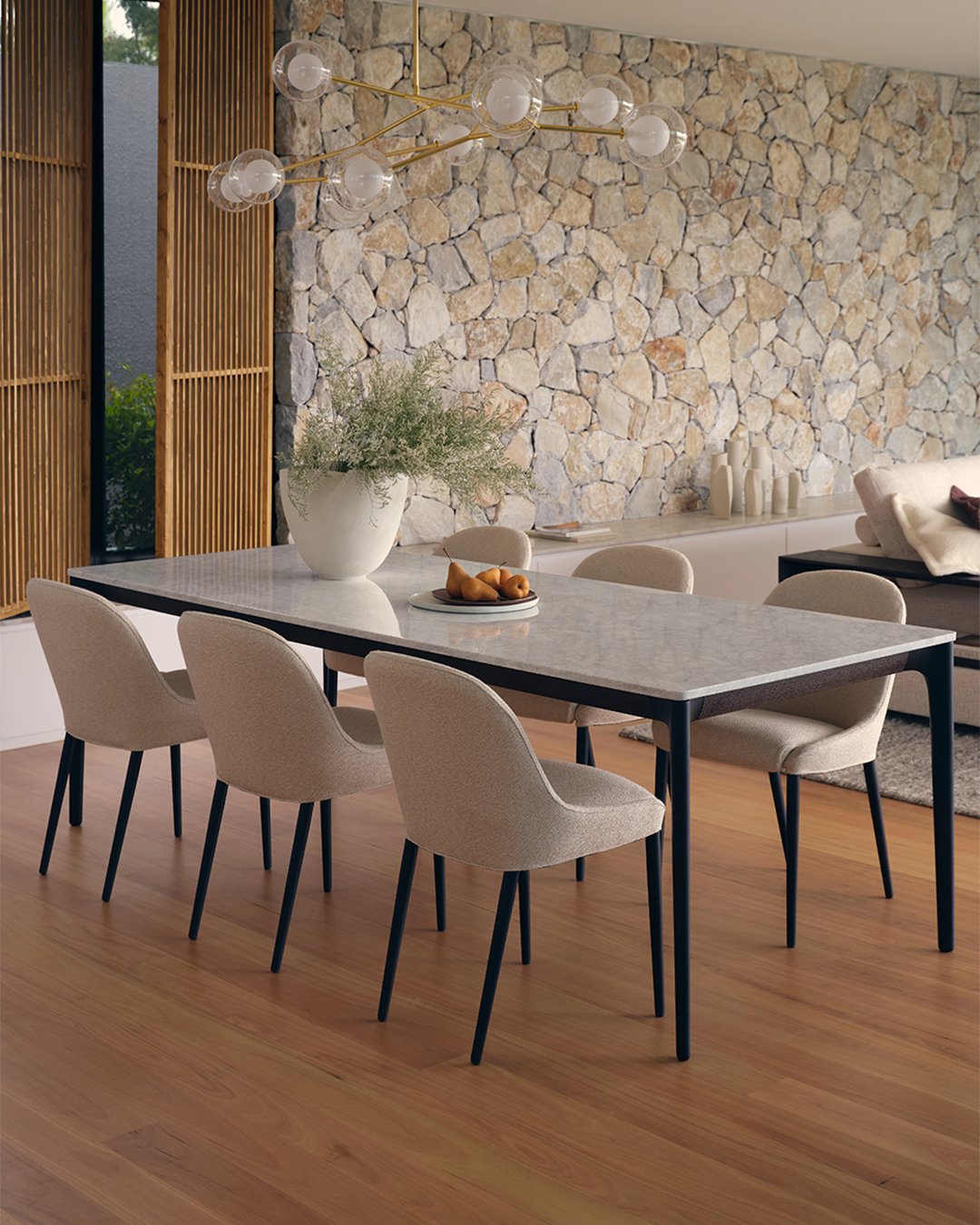 Rectangular white stone dining table with cream chairs and stone feature wall