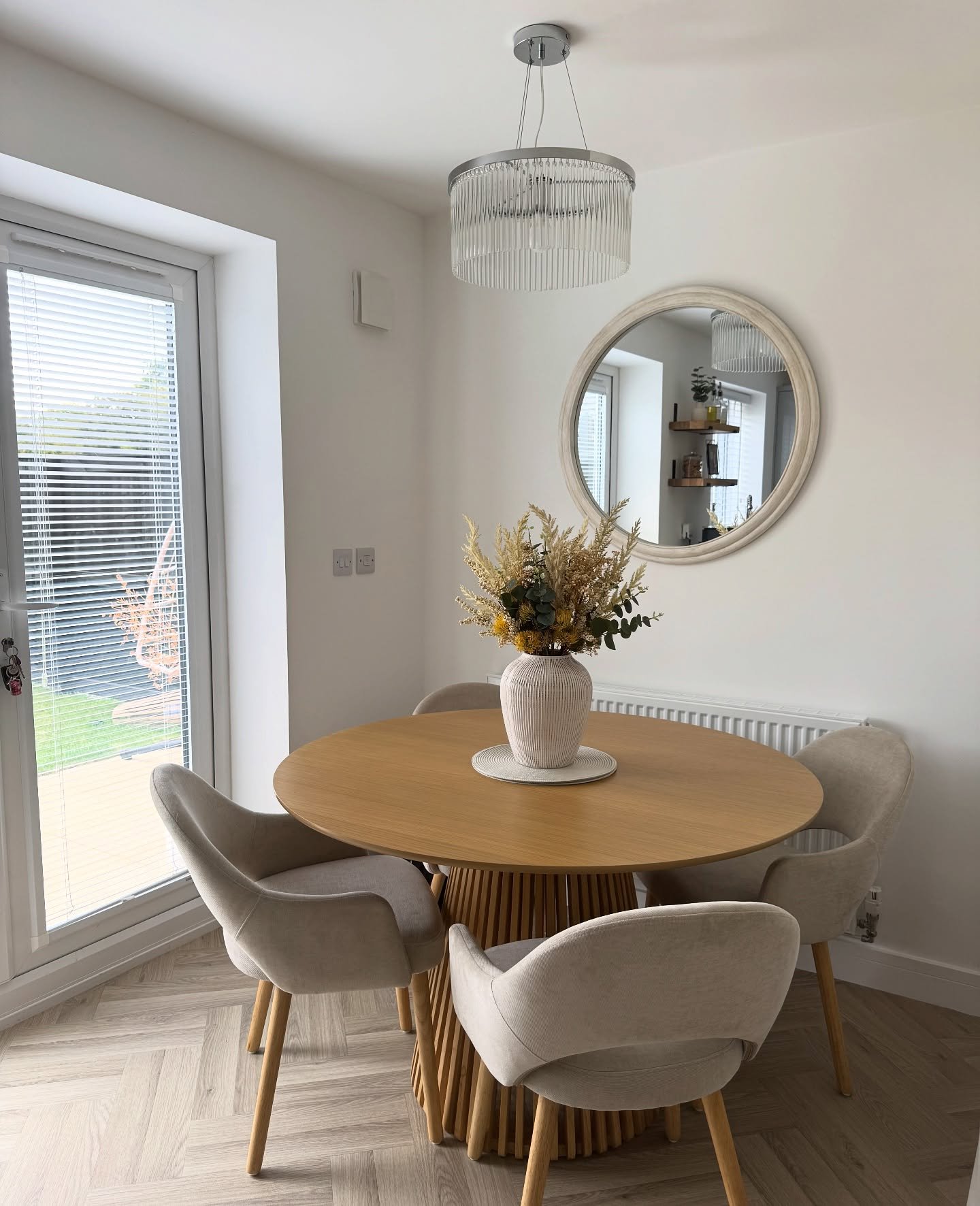 Round light wood dining table with slatted cone base and beige velvet chairs