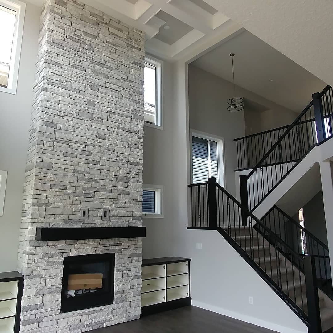 Vaulted living room with a massive, floor-to-ceiling fireplace column clad in light gray stacked stone veneer with a black wood mantel.