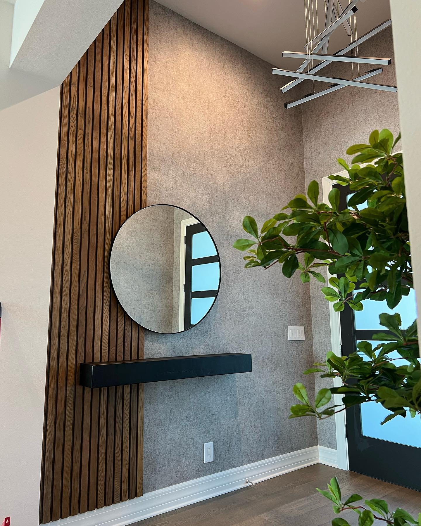 Entryway accent wall featuring vertical wood slats, grey wallpaper, and a round mirror.