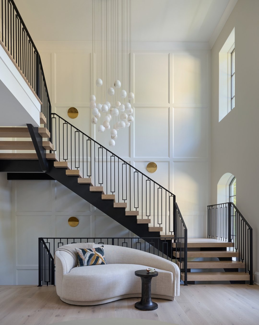 Large white staircase wall featuring floor-to-ceiling grid board and batten paneling with brass accents and a modern chandelier.