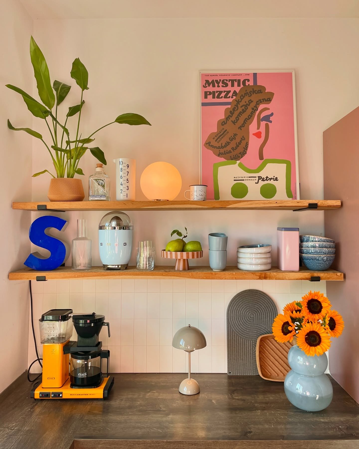 Kitchen open wooden shelves with Mystic Pizza poster and colorful appliances