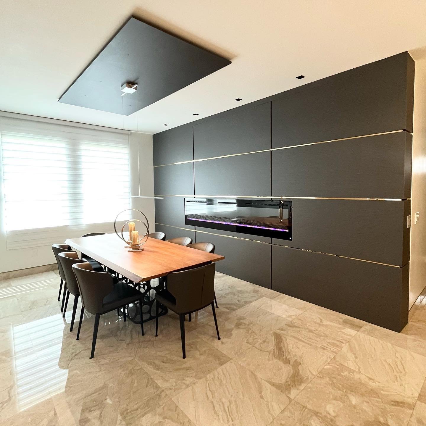 Dark grey dining accent wall featuring horizontal brass strips and a built-in linear fireplace.