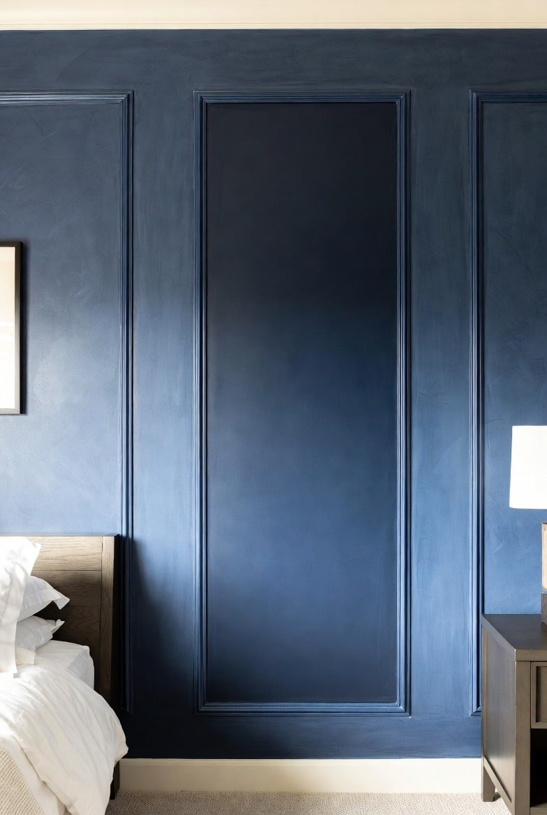 Navy blue accent wall featuring picture frame molding with brushed suede texture behind dark wood furniture