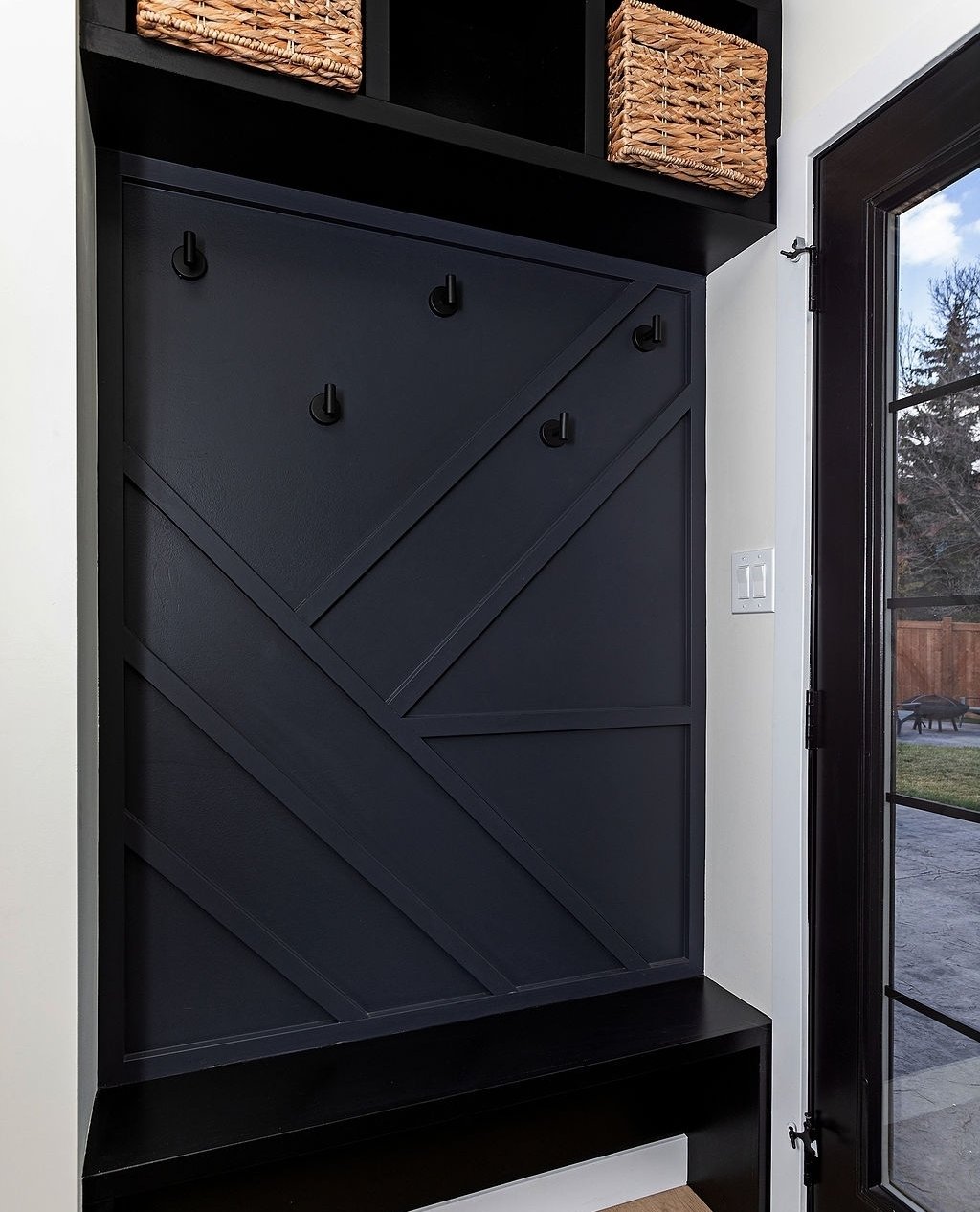 Built-in entryway hall tree featuring dark navy geometric shiplap, black bench, wall hooks, and upper cubbies with woven baskets.