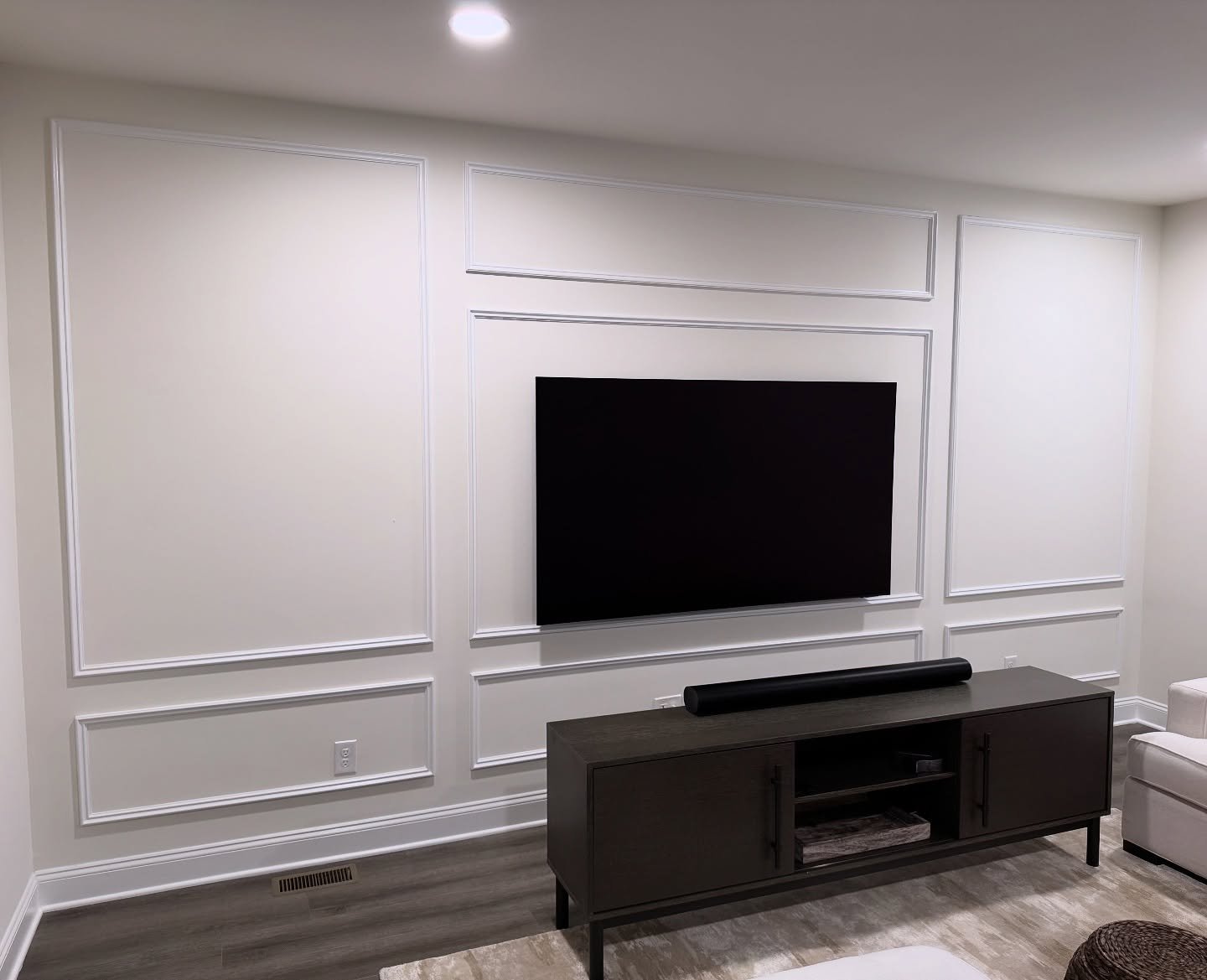 White wall with picture frame molding and dark wood media console.