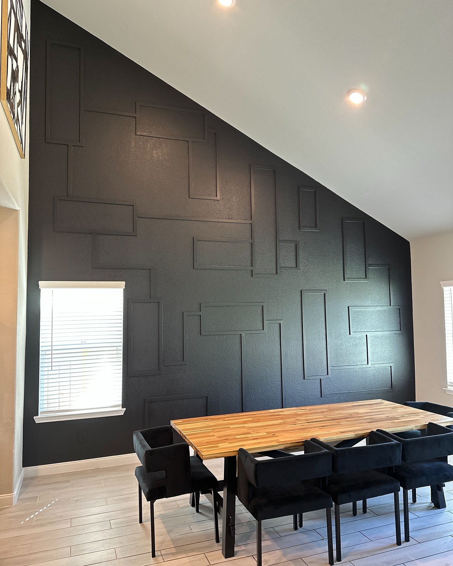 Black dining room accent wall featuring asymmetrical geometric molding on a high vaulted ceiling.