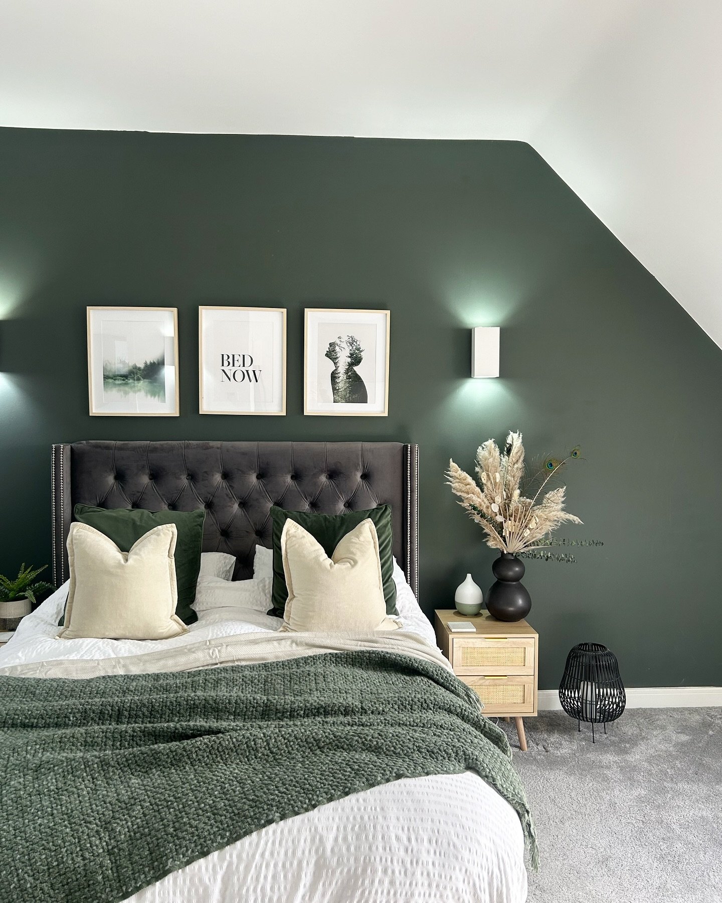 Dark green bedroom accent wall with slanted ceiling featuring three framed art prints and wall sconces