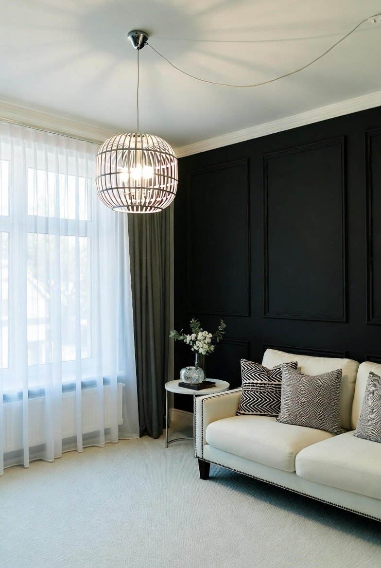 Living room with a paneled Black Accent Wall, large globe pendant light, and cream sofa.